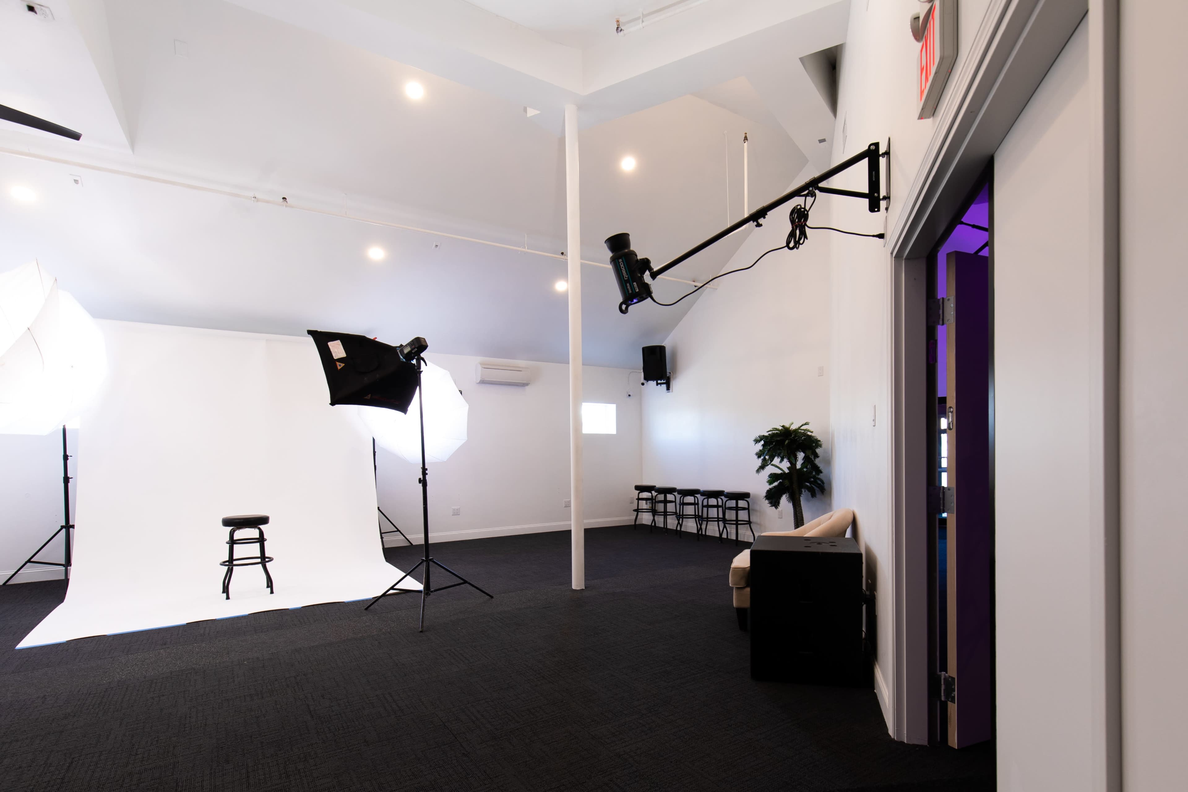 A photography studio with a white backdrop, a stool, softbox lighting, and a small seating area.