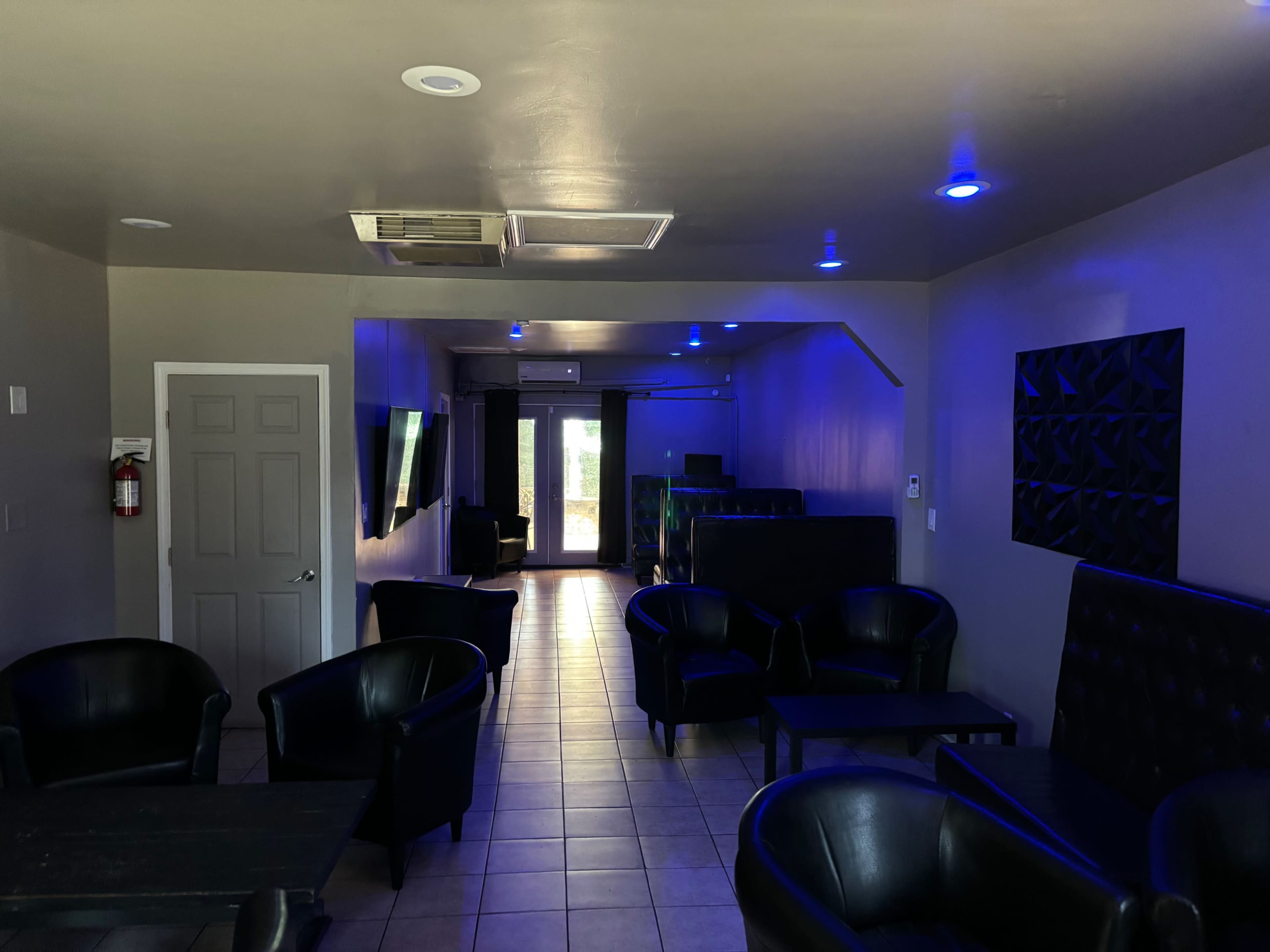 The image shows a dimly lit lounge area with black chairs arranged around tables and blue lights illuminating the space.
