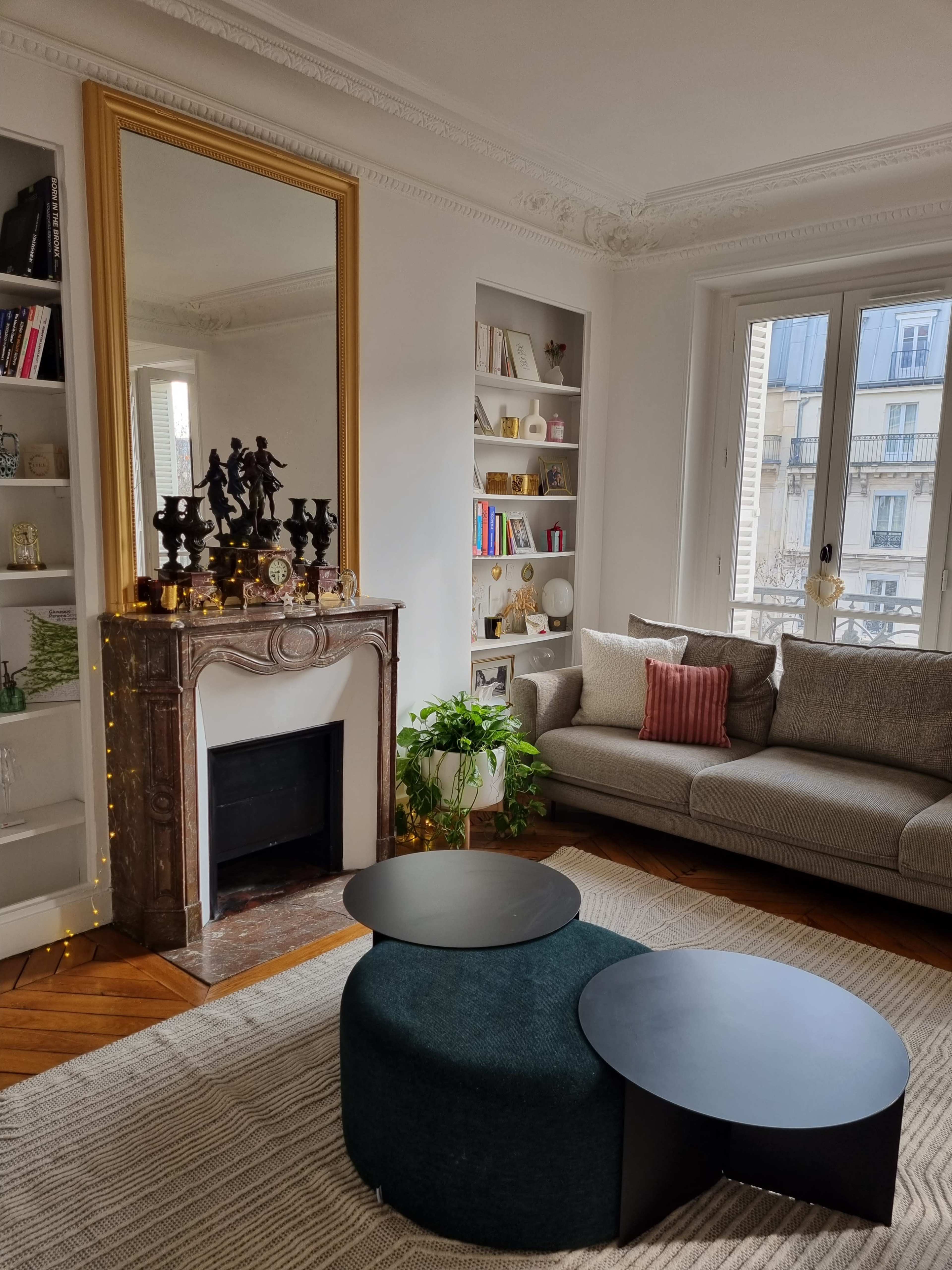A living room with a fireplace, a large mirror, a comfortable gray sofa, and two circular coffee tables on a textured rug.