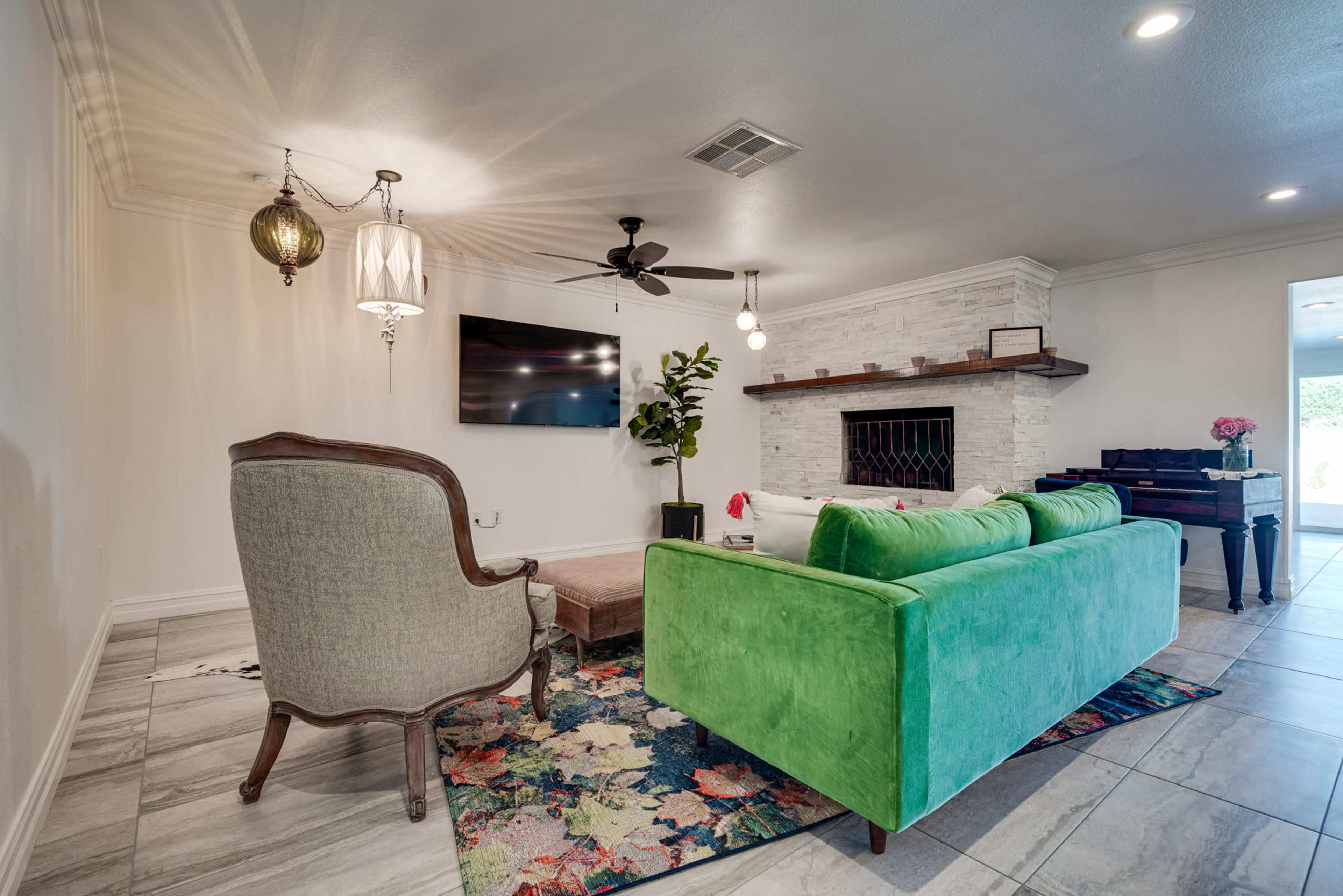 A modern living room featuring a green couch, a decorative armchair, a flat-screen TV on the wall, and a light-colored stone fireplace.