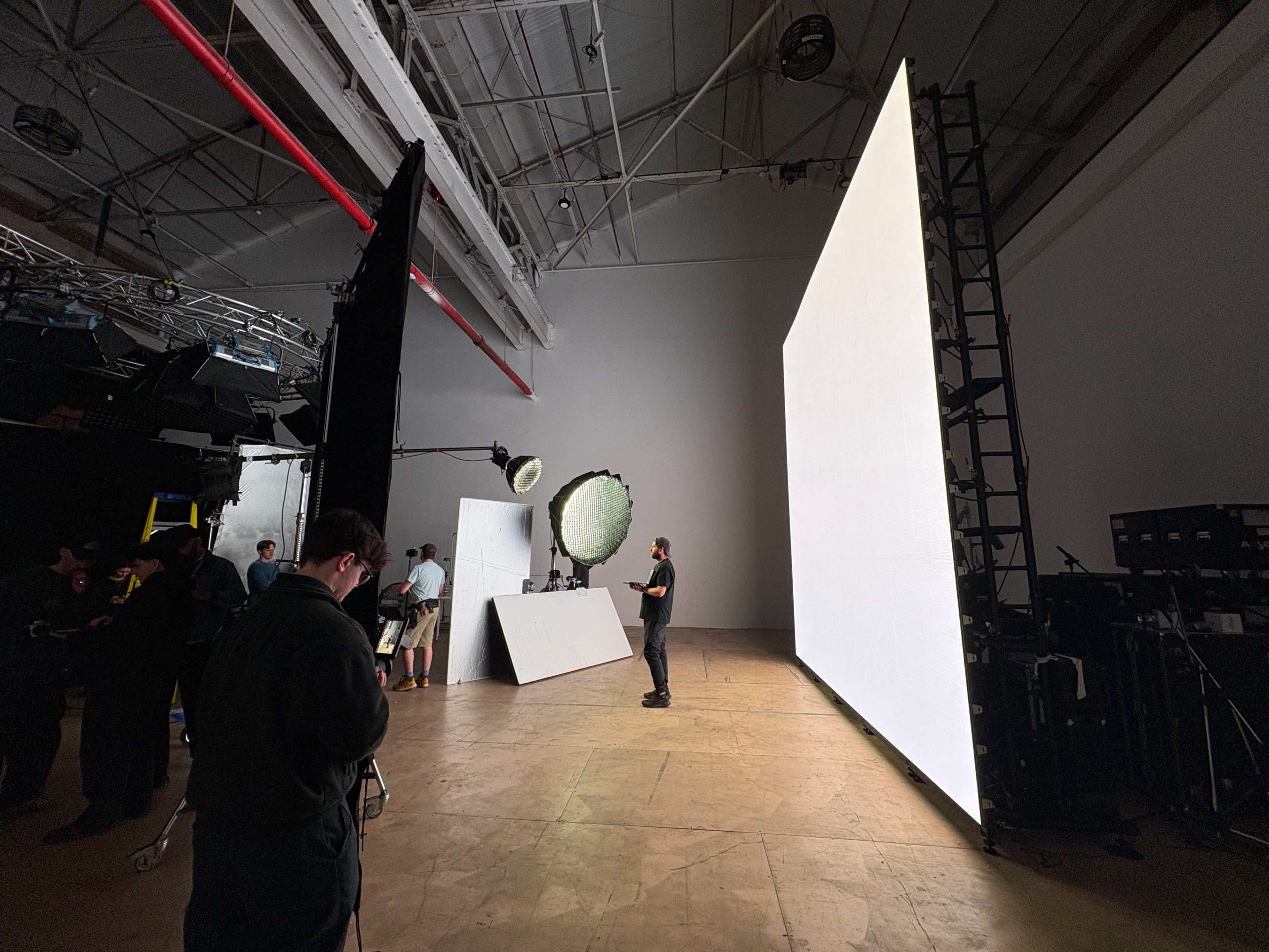 A film studio is set up with a large white backdrop, lighting equipment, and crew members preparing for a shoot.