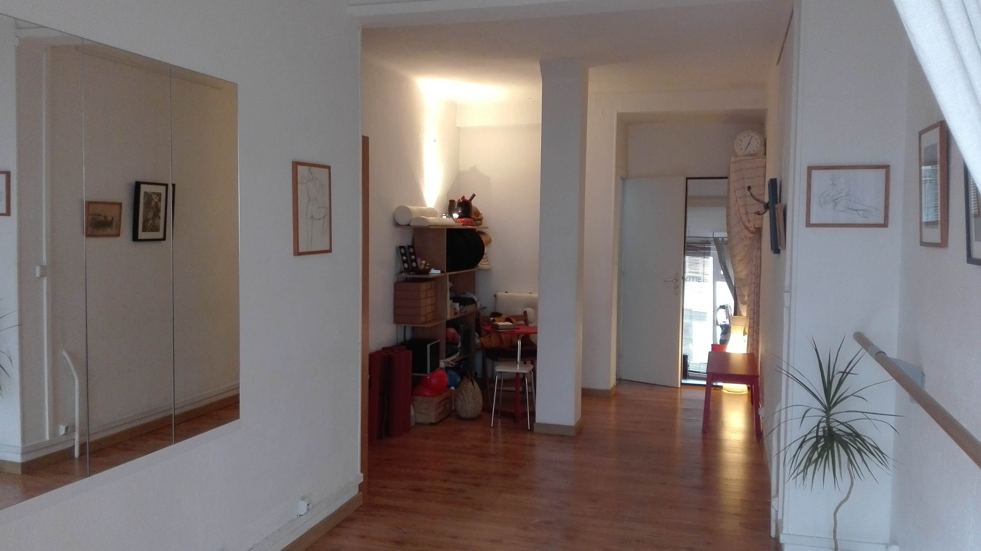 A bright hallway with a large mirror on the left, storage bins and a chair on the right, and a doorway leading outside at the far end.