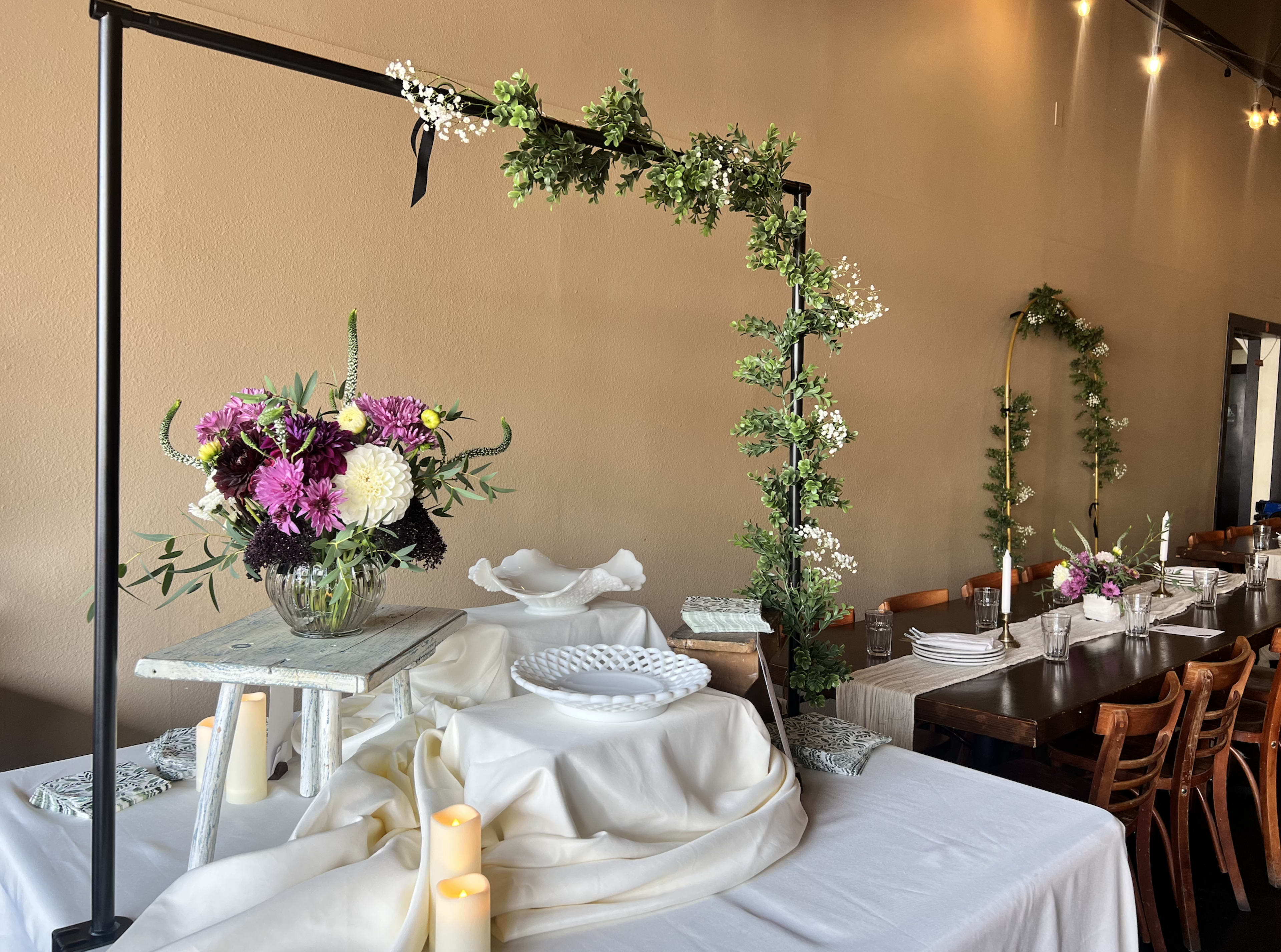 A decorated dining area features floral arrangements on a table with a backdrop of green foliage and white accents.