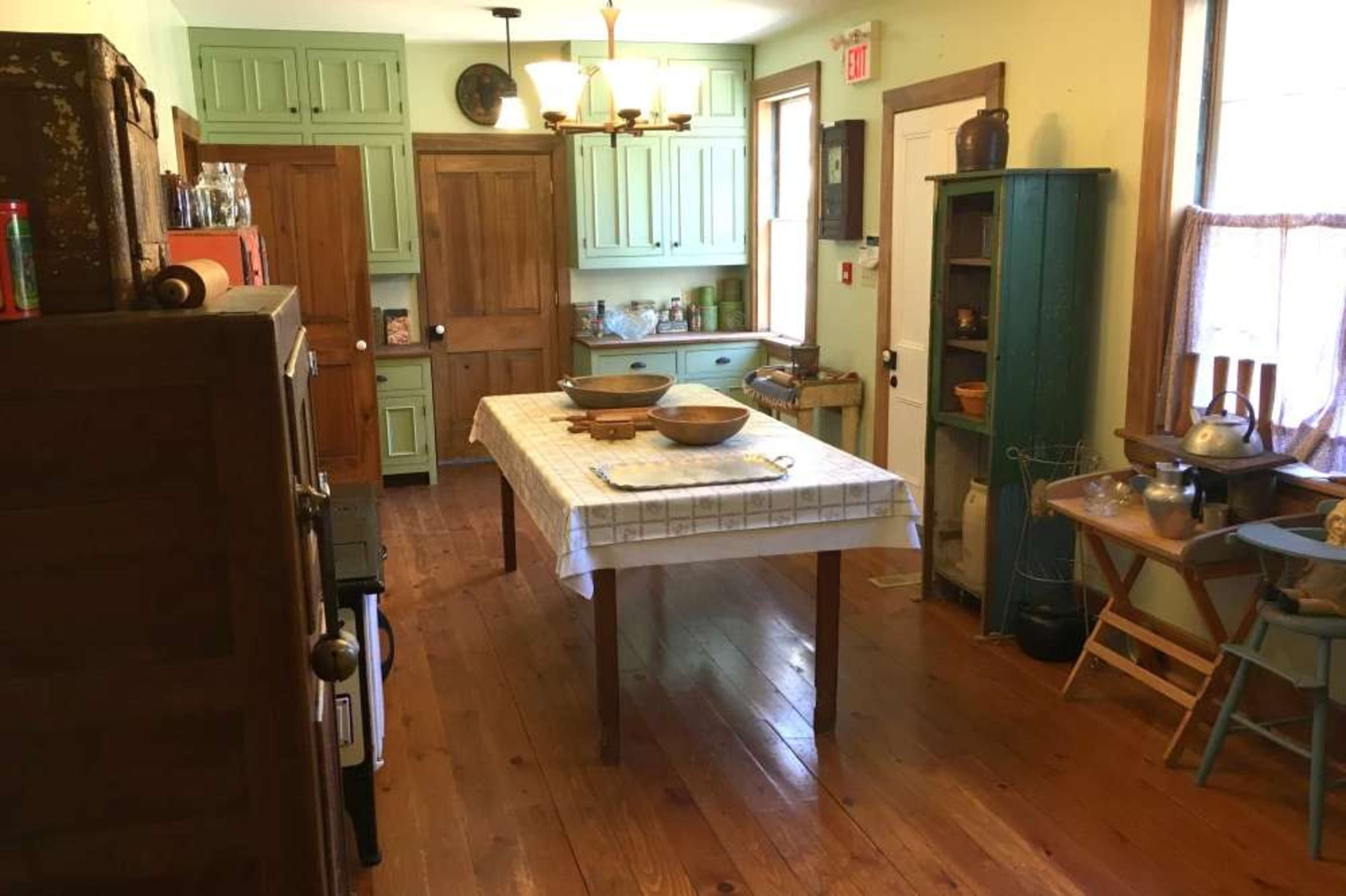 A quaint kitchen with wooden floors, a central table, and green cabinetry along the walls.