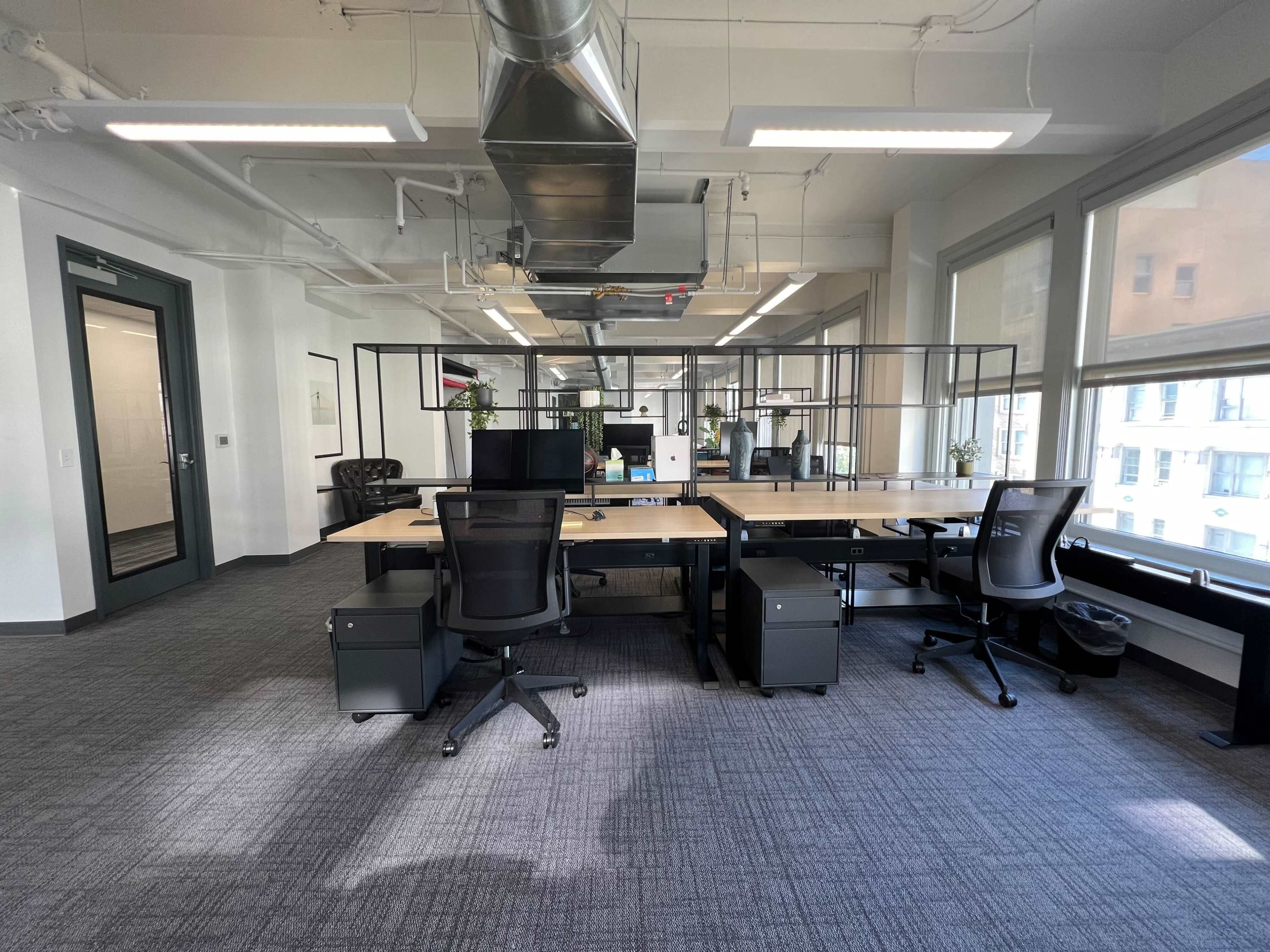 A modern office space with two desks facing each other, surrounded by glass partitions and equipped with ergonomic chairs and computer monitors.
