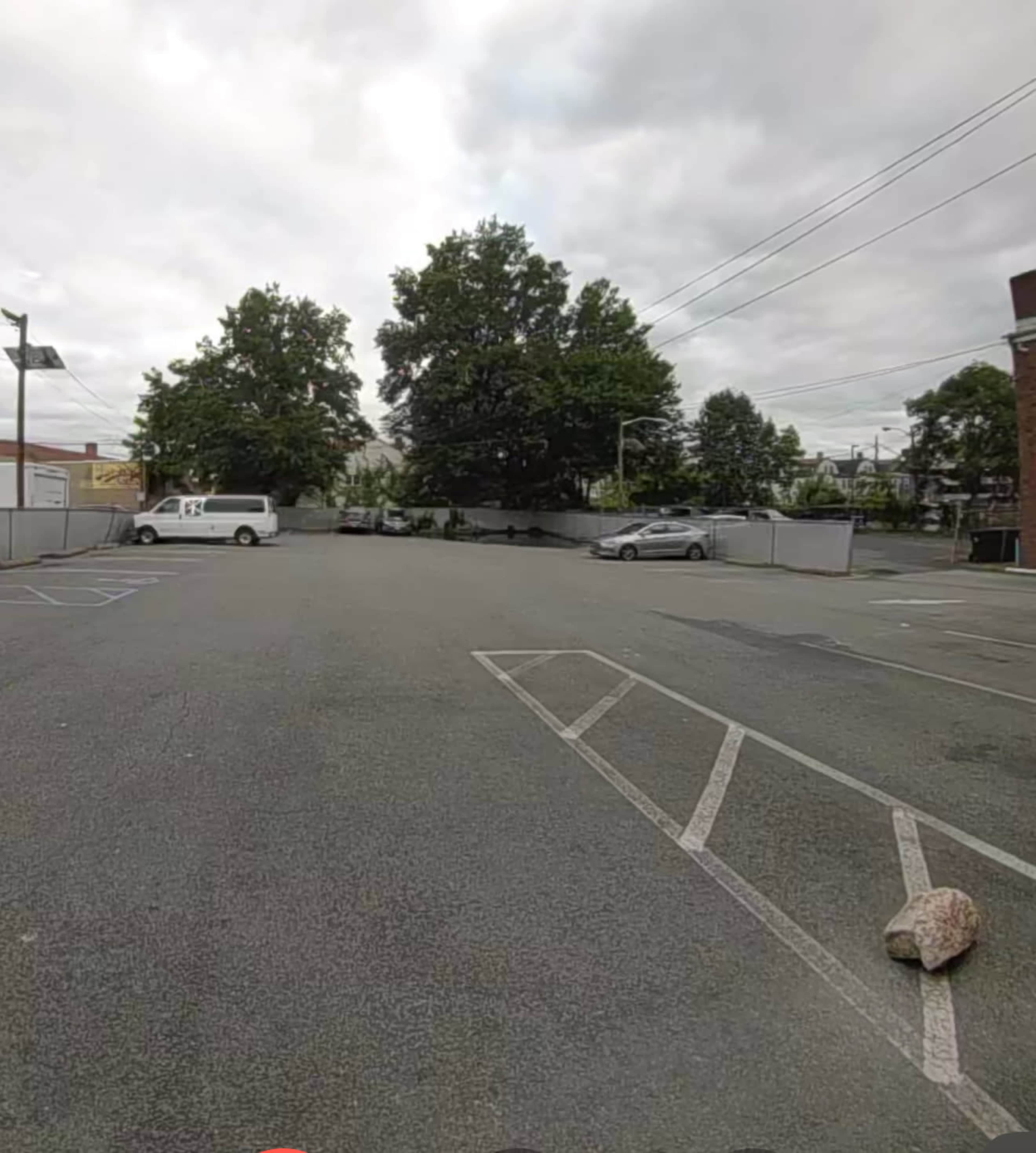 A nearly empty parking lot with several parked cars and a large tree in the background.