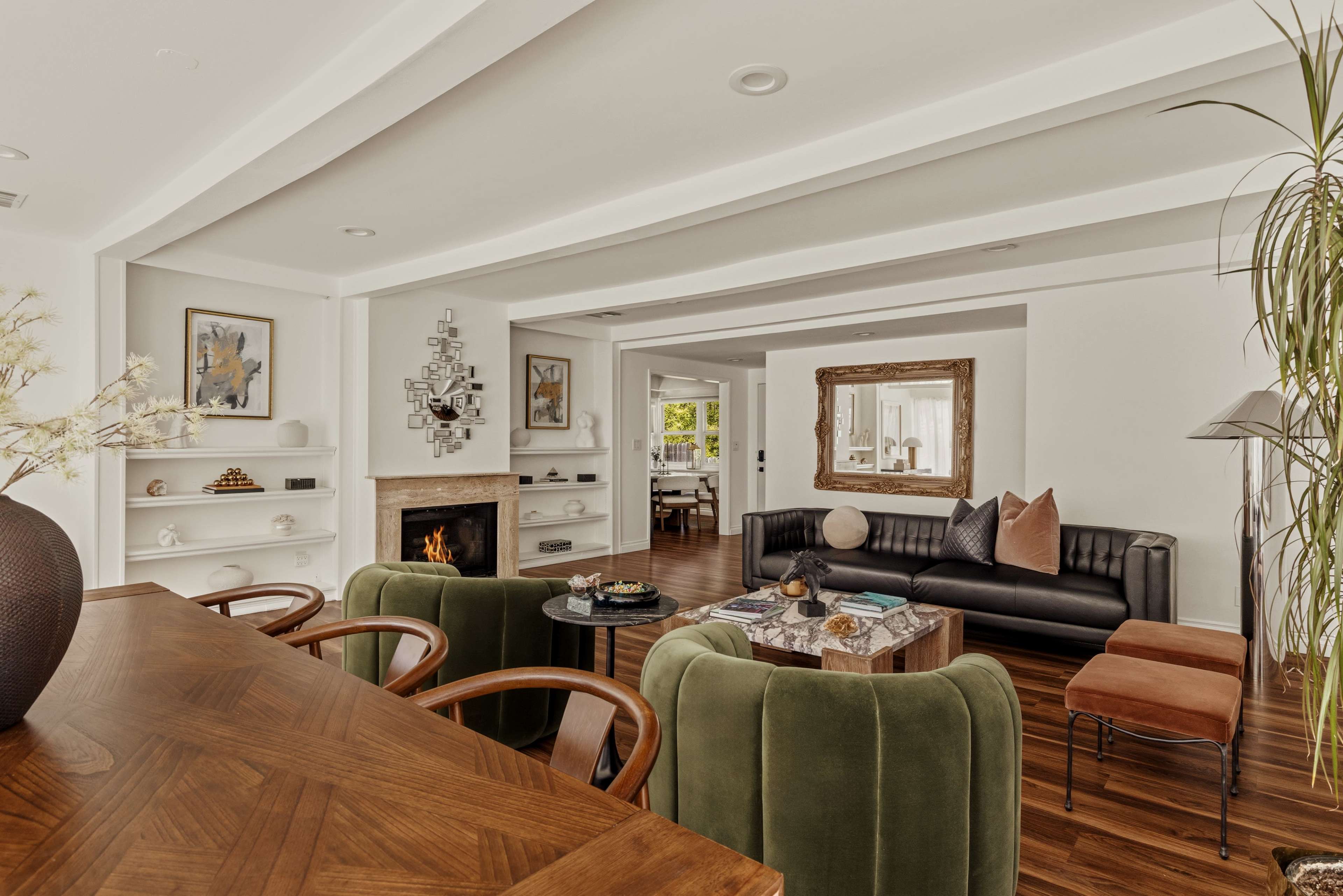 The image shows a modern living space with a dining area featuring a wooden table and green upholstered chairs, a black leather sofa, and a cozy fireplace in an open layout.