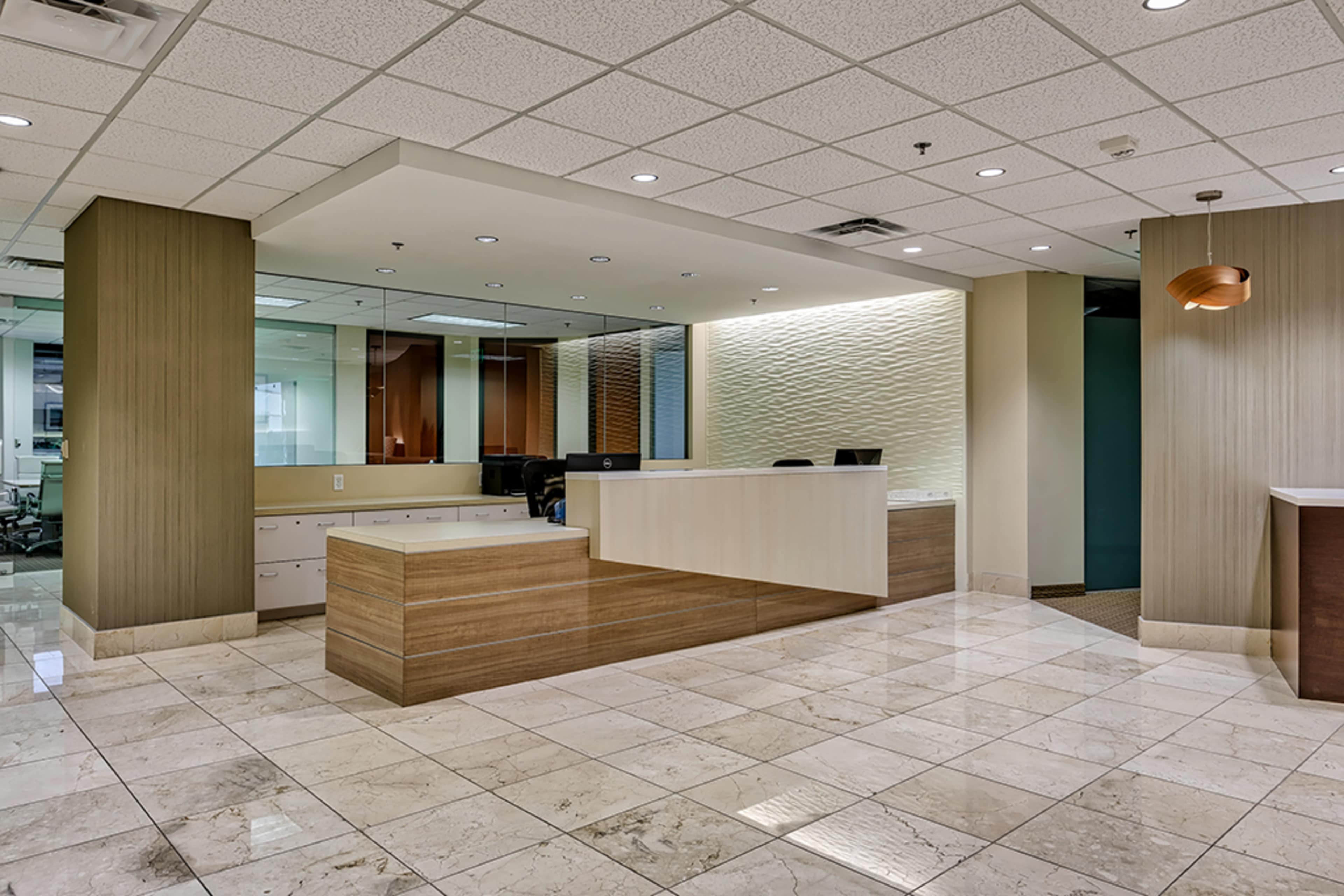 A modern office reception area with a wooden front desk, polished marble flooring, and a softly lit wall backdrop.