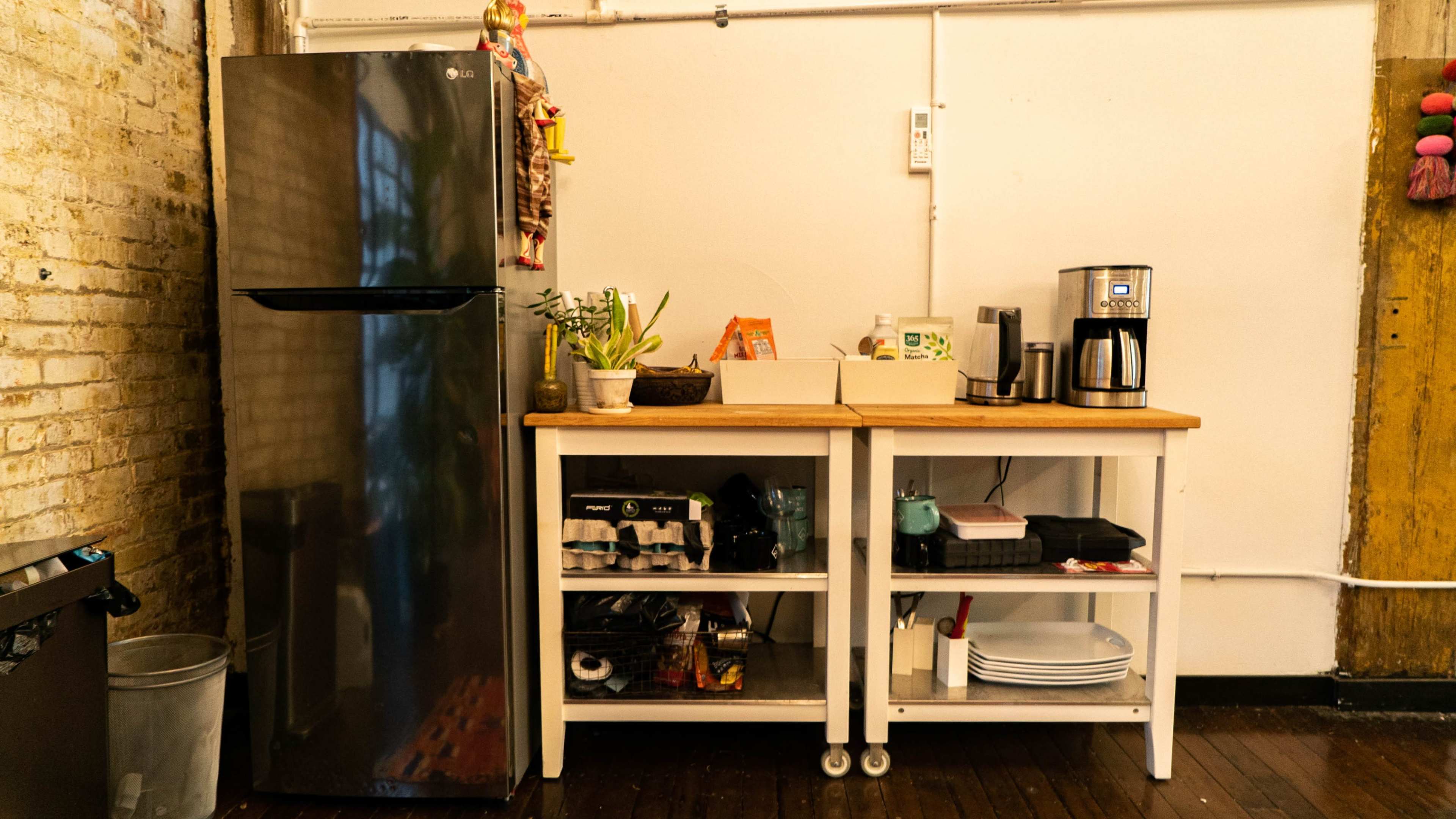 The image shows a kitchen area featuring a stainless steel refrigerator, a coffee maker, and a countertop with various kitchen utensils and supplies.