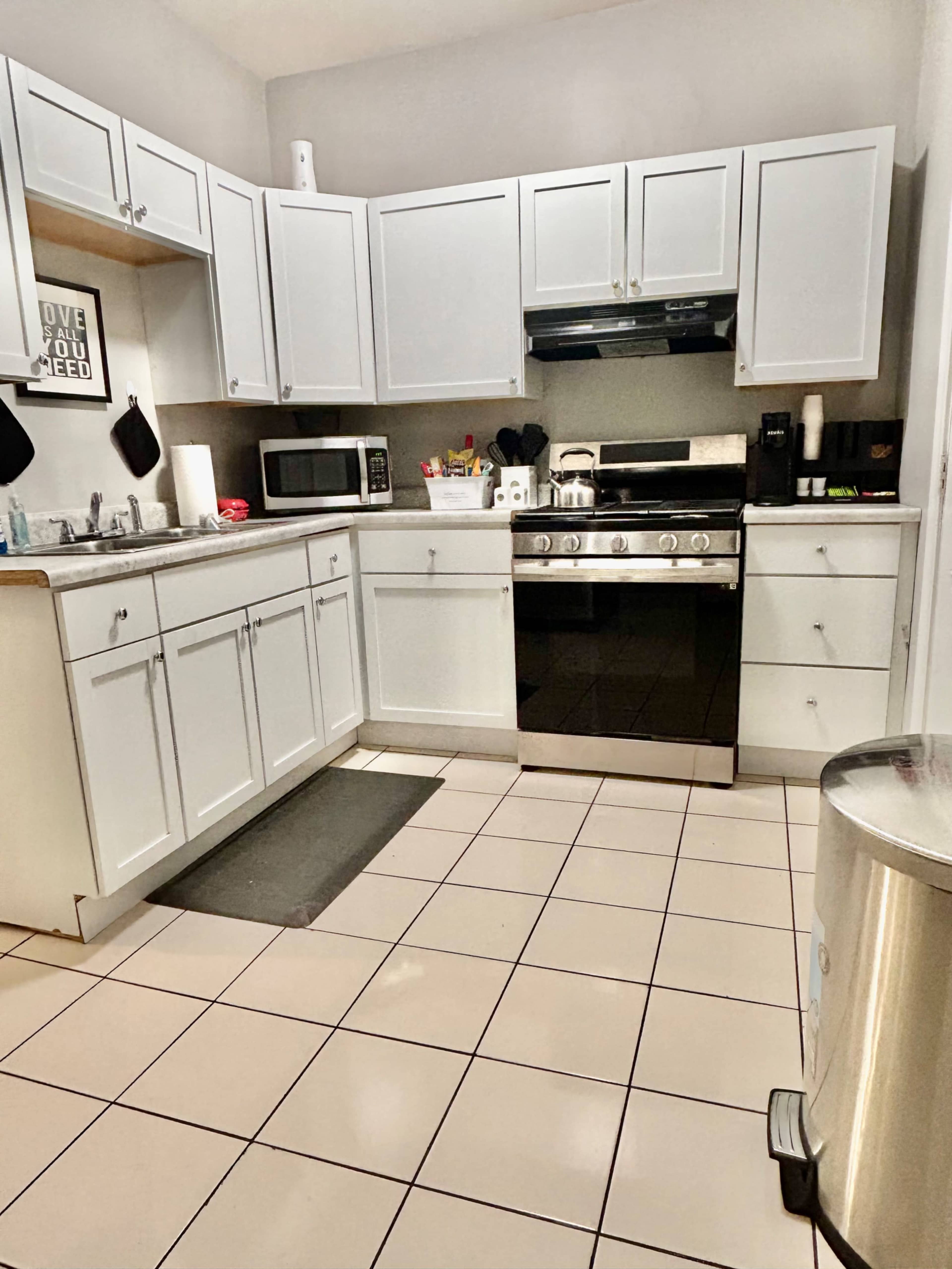 A clean kitchen features white cabinets, stainless steel appliances, and tiled flooring.