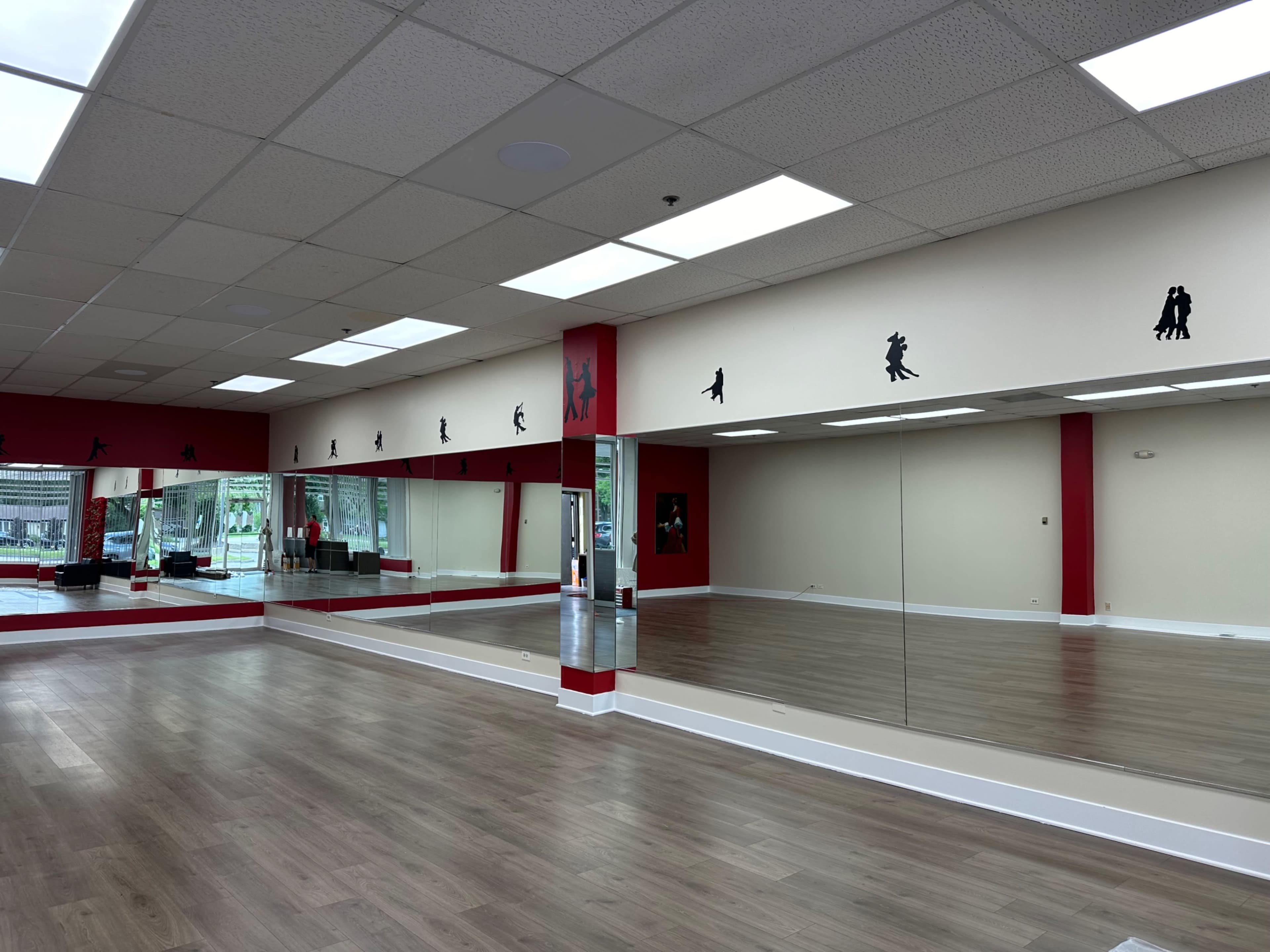 A dance studio with wooden flooring, mirrored walls, and silhouettes of dancers along the upper section of the walls.