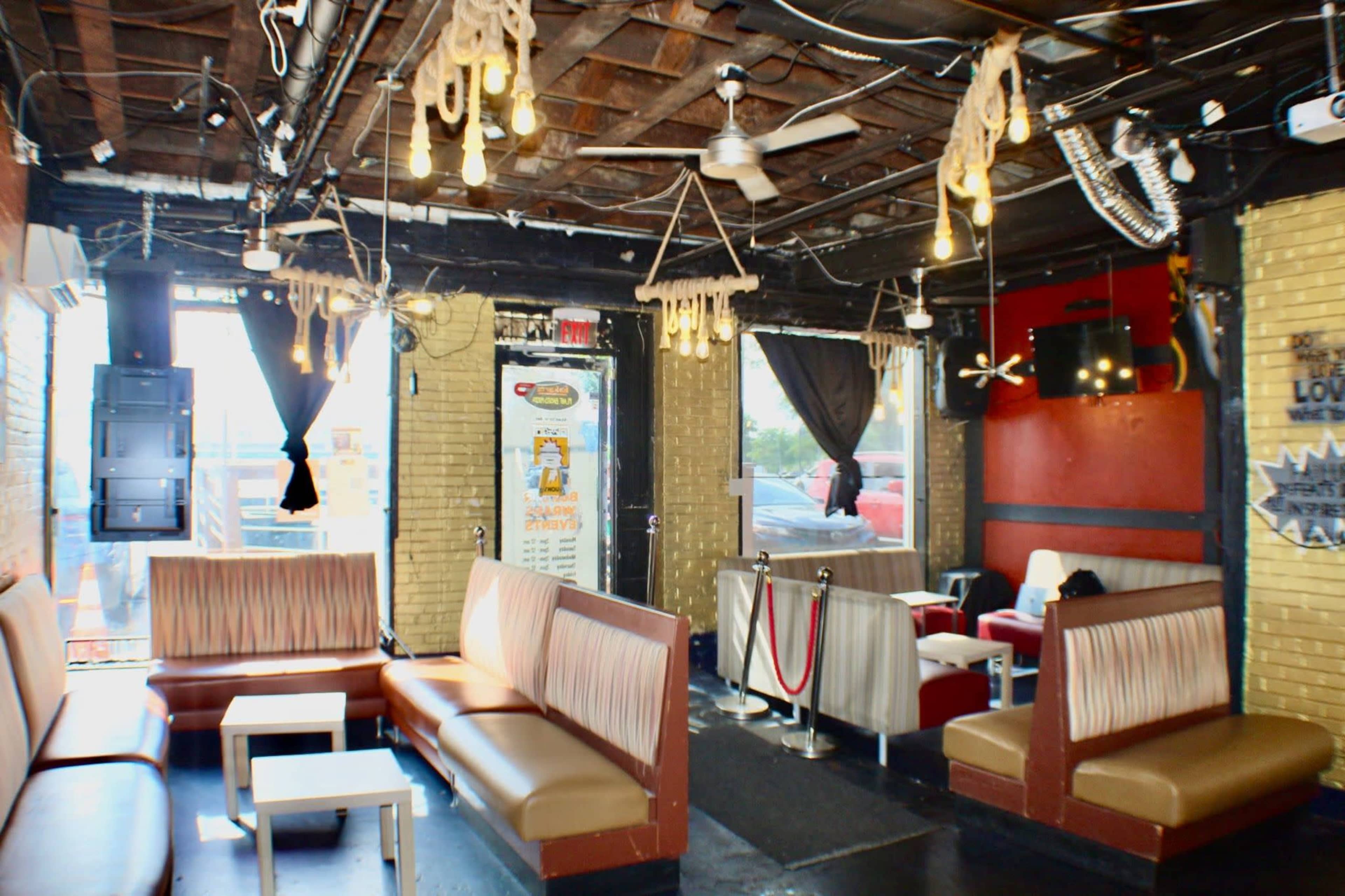 The image shows a bar or lounge area with seating, exposed brick walls, and hanging light fixtures.
