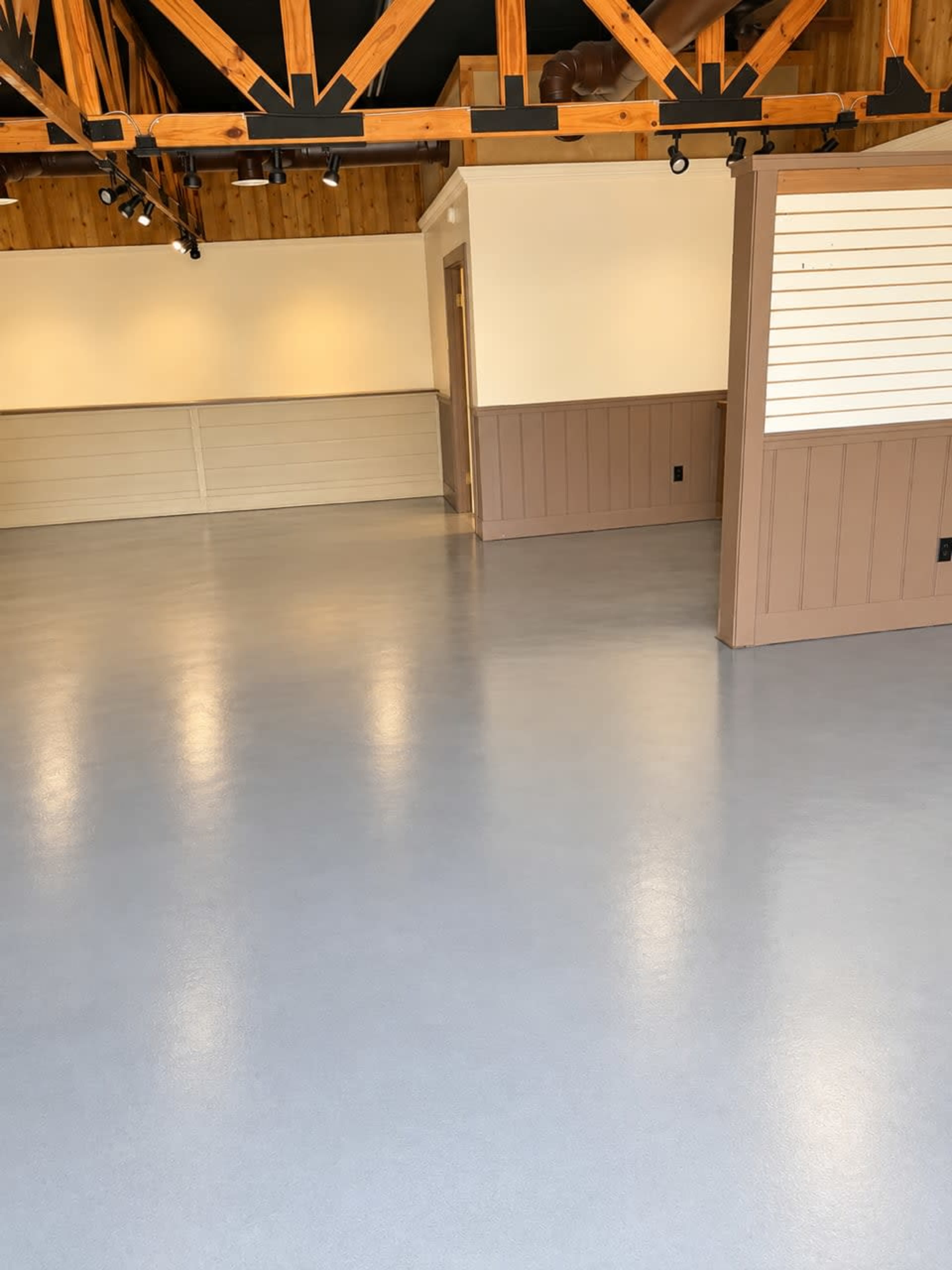 The image shows a spacious interior with a polished blue-gray floor and wooden beams on the ceiling.