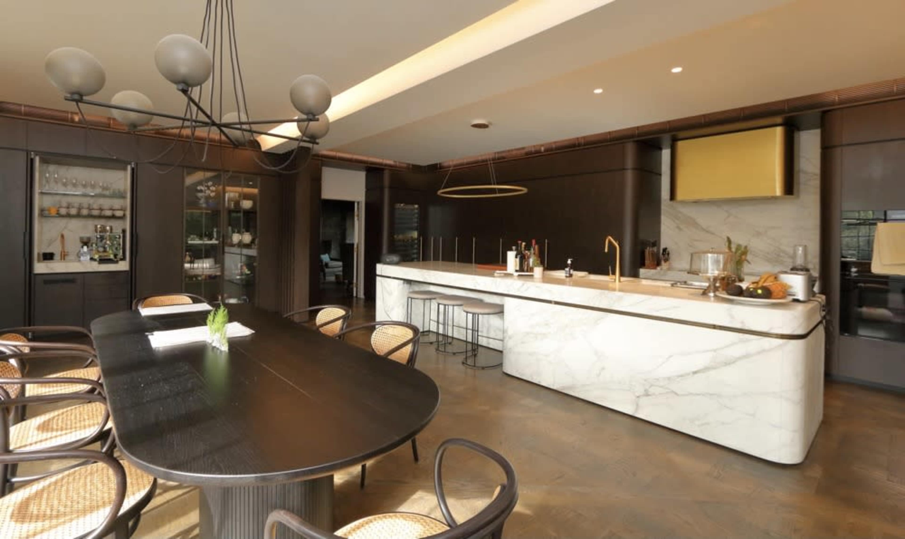 A modern kitchen features dark cabinetry, a marble island, and a large dining table surrounded by woven chairs.