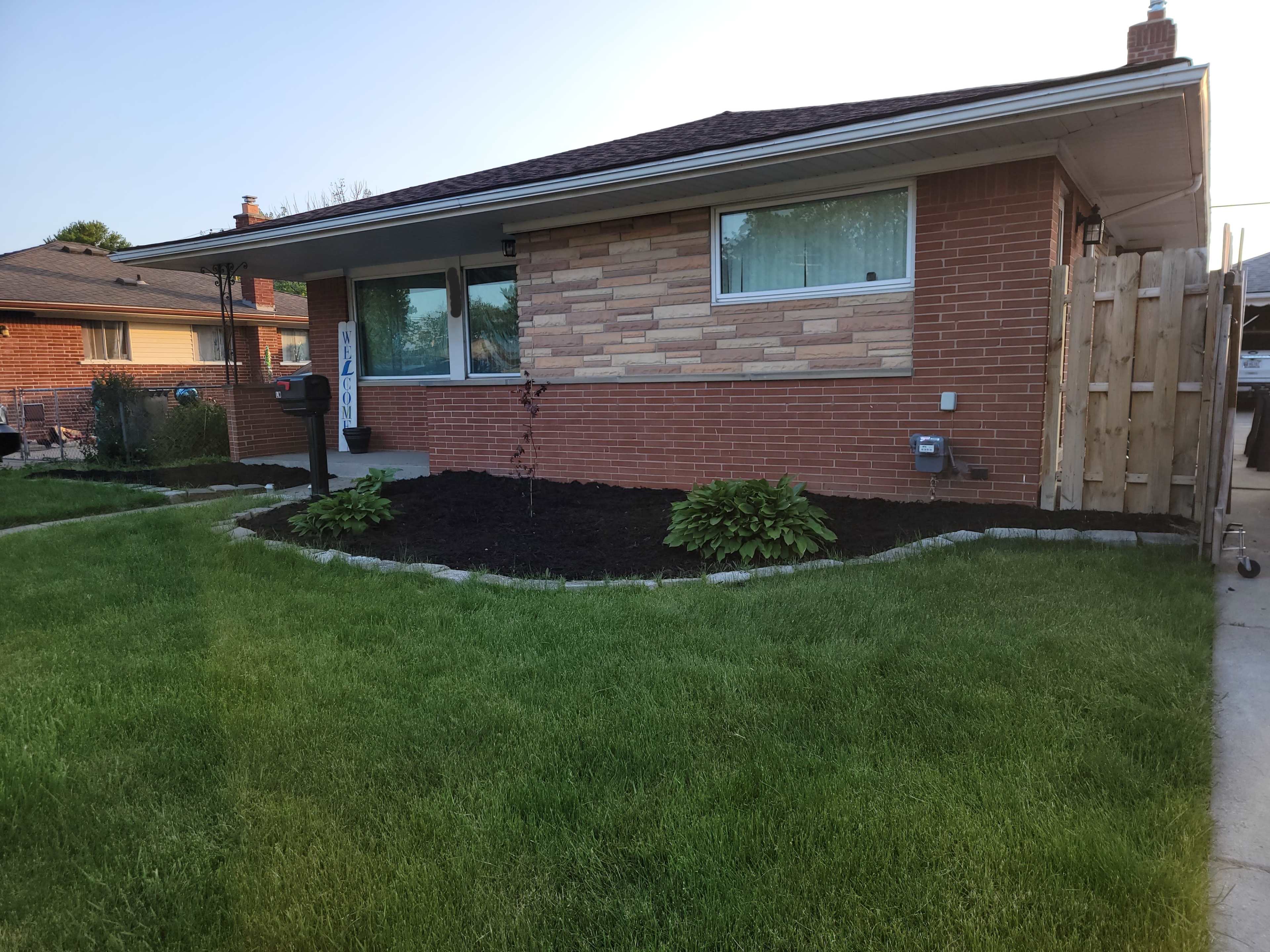 The image shows a single-story brick house with a landscaped front yard featuring trimmed grass and plants along the border.