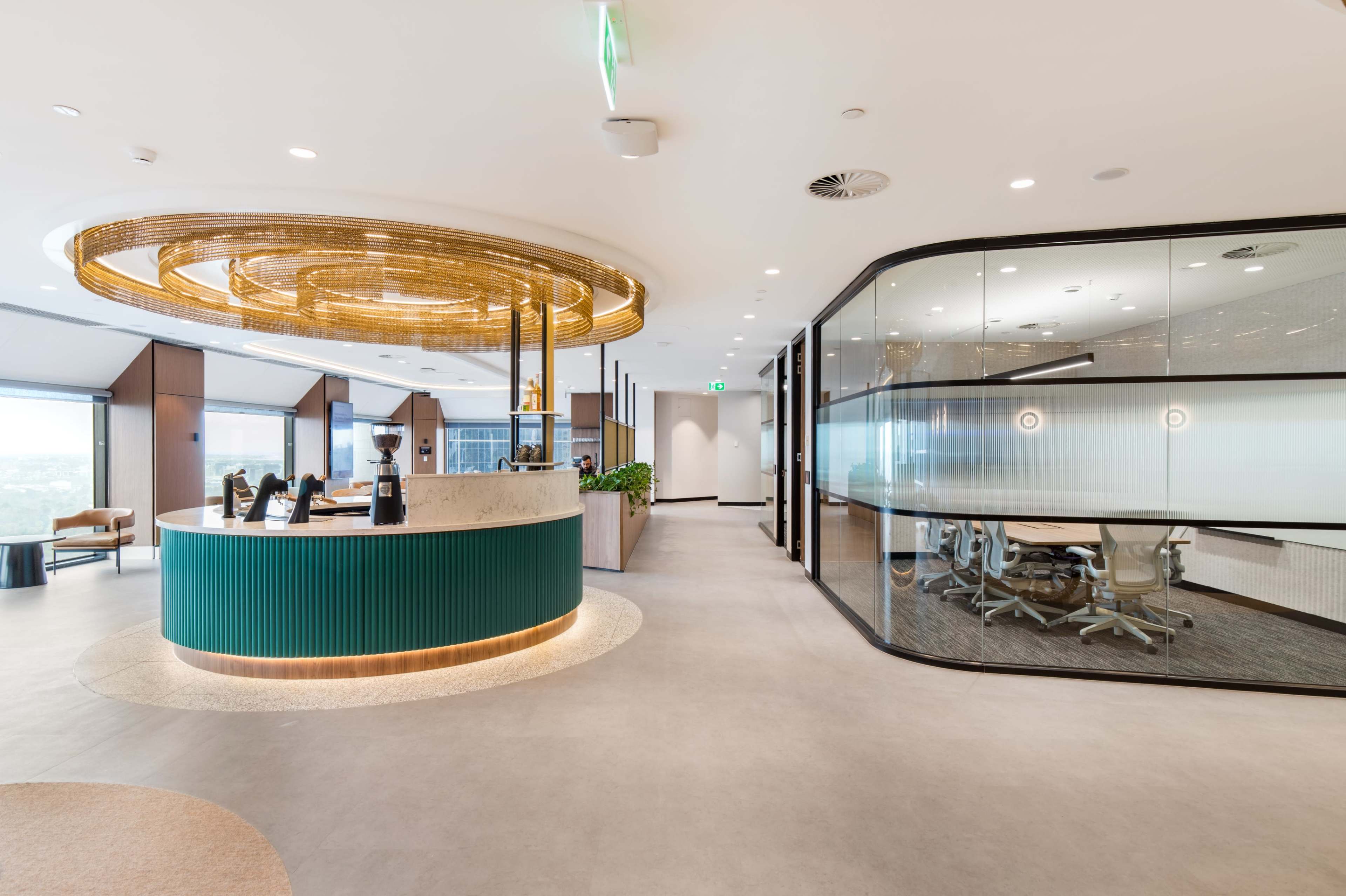 The image shows a modern office space featuring a circular reception area with a green and stone counter, leading to a glass-walled meeting room.