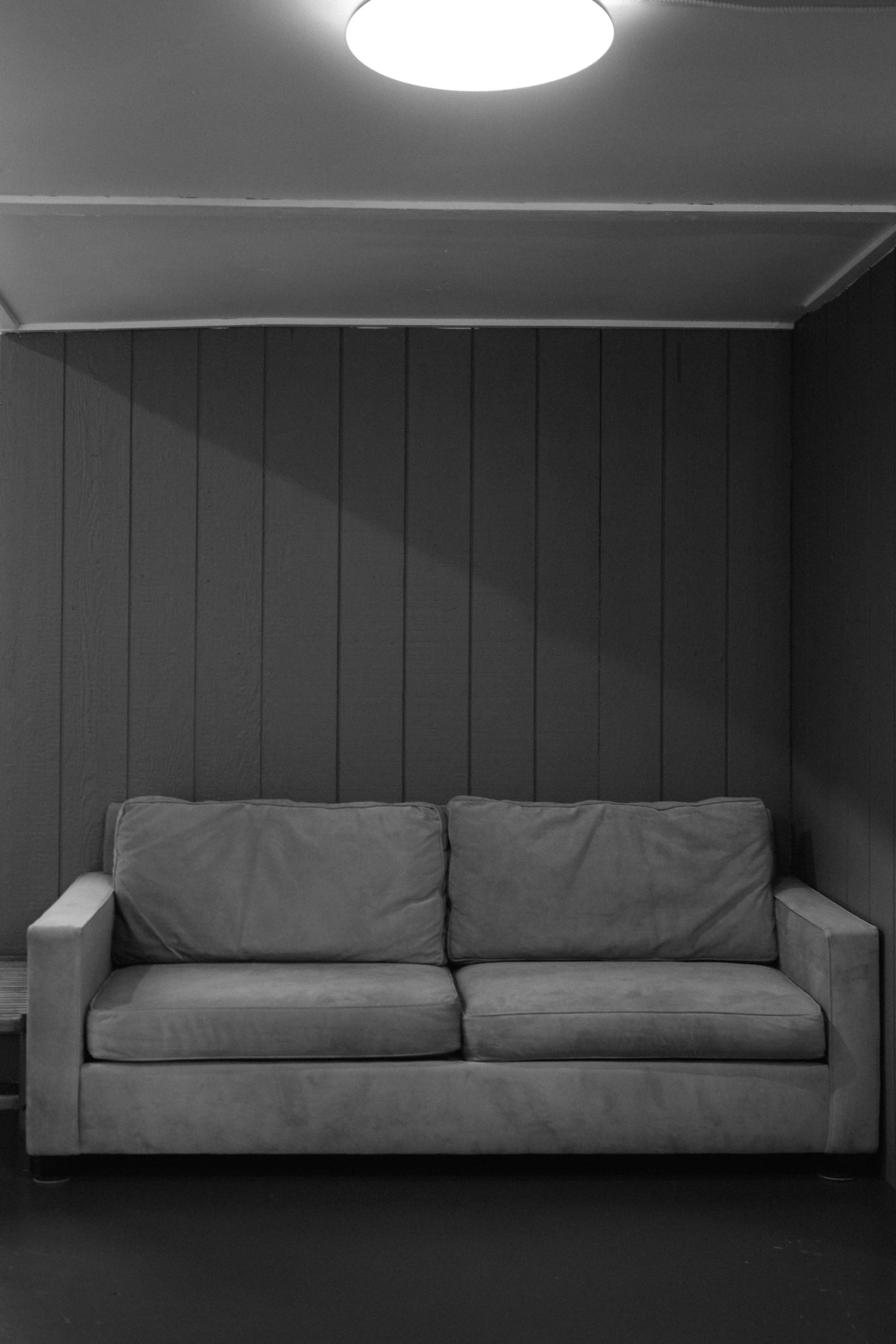 A gray sofa is placed against a dark wooden wall under a round ceiling light.