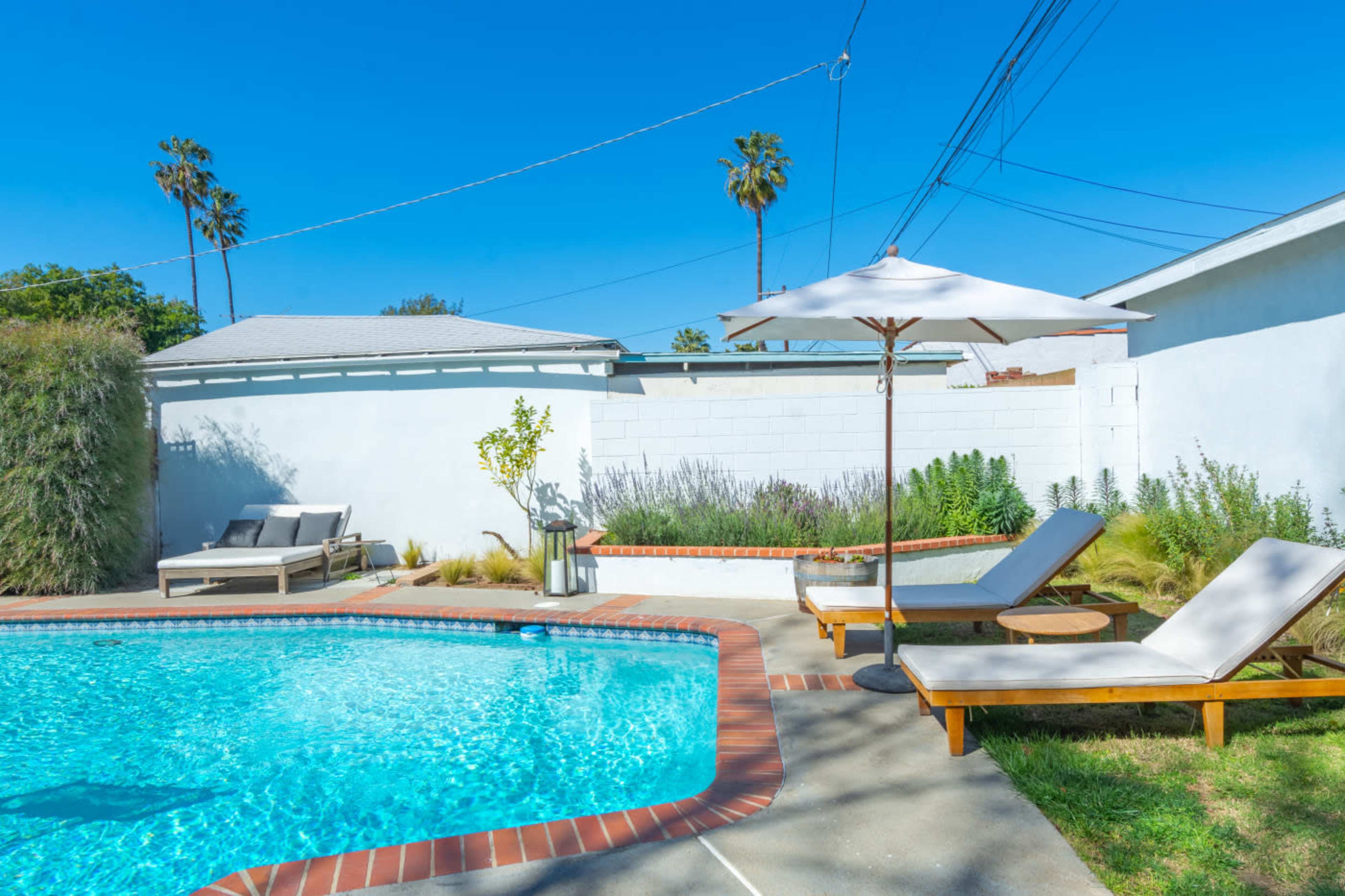 A swimming pool surrounded by lounge chairs and landscaped greenery under a clear blue sky.