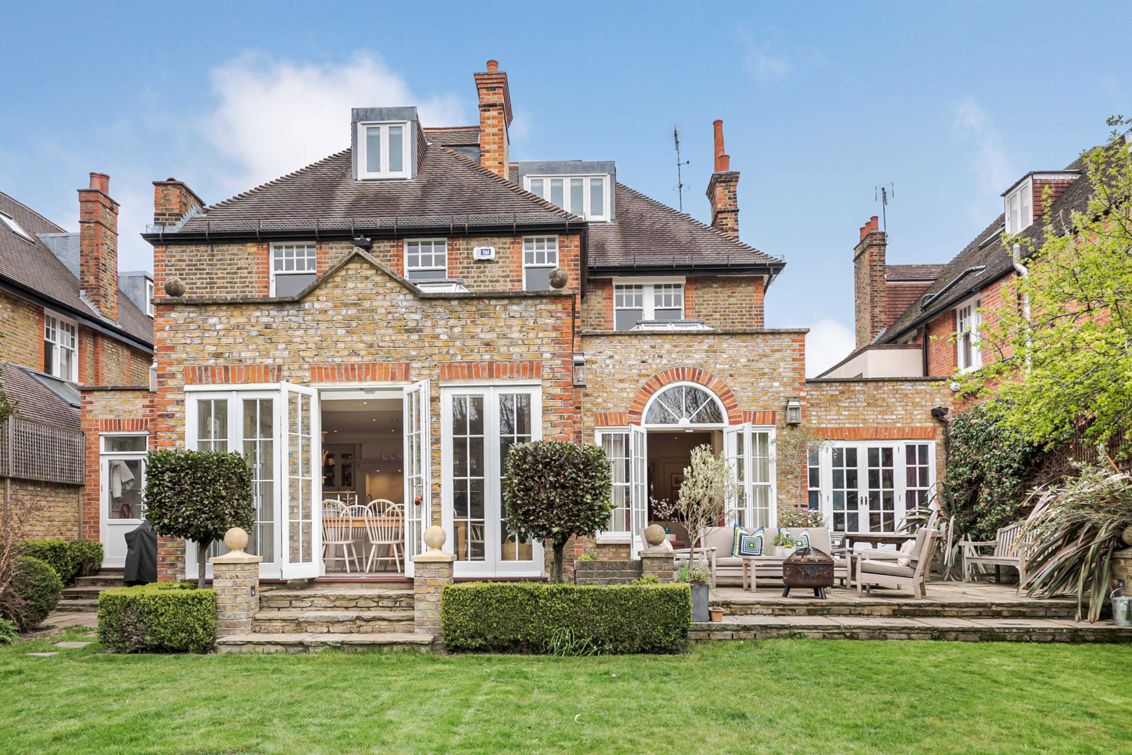 A brick house with large windows and a garden sits surrounded by other residential buildings.