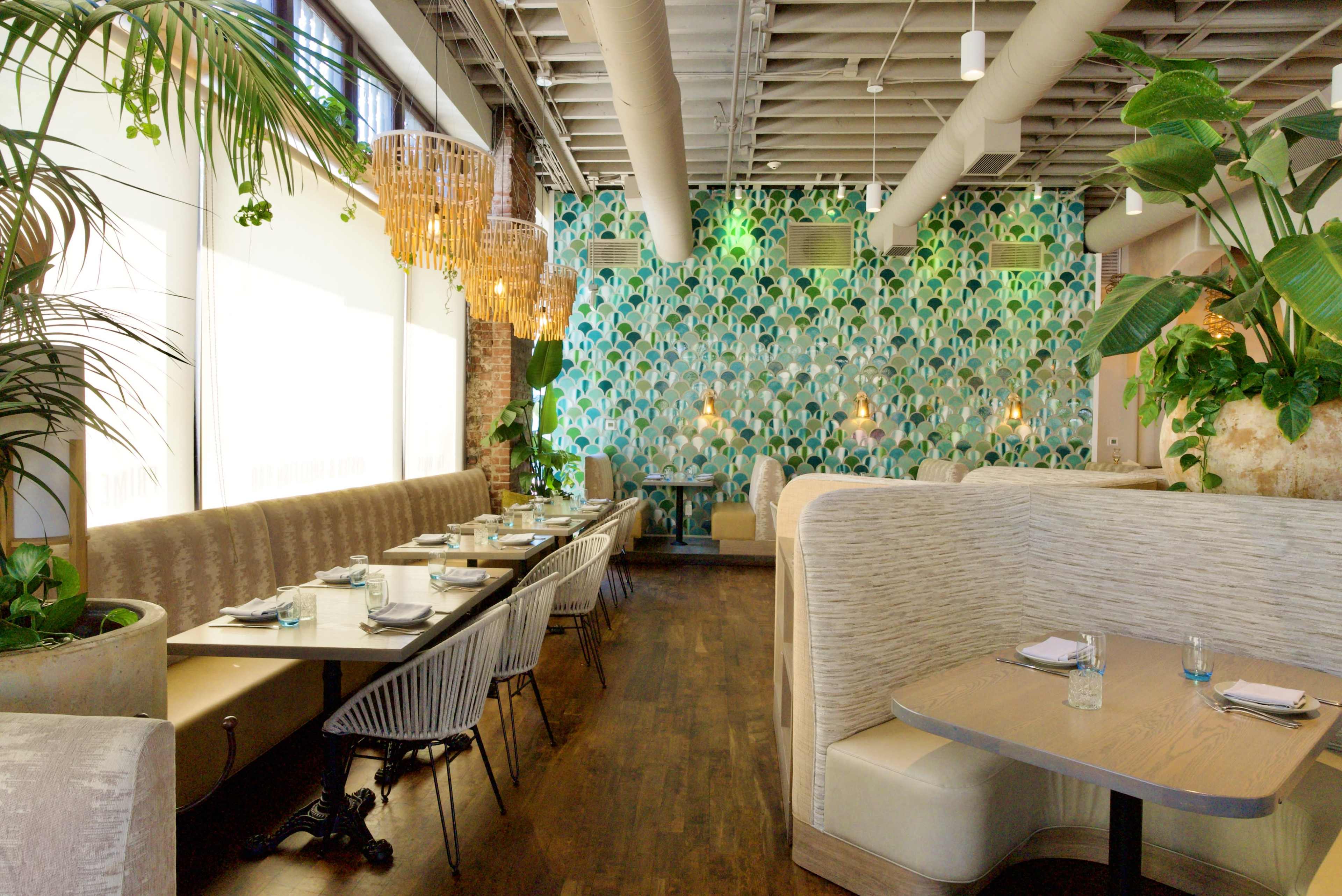 The image shows a modern restaurant interior featuring booth seating, a vibrant green wall with decorative lighting, and large plants throughout the space.
