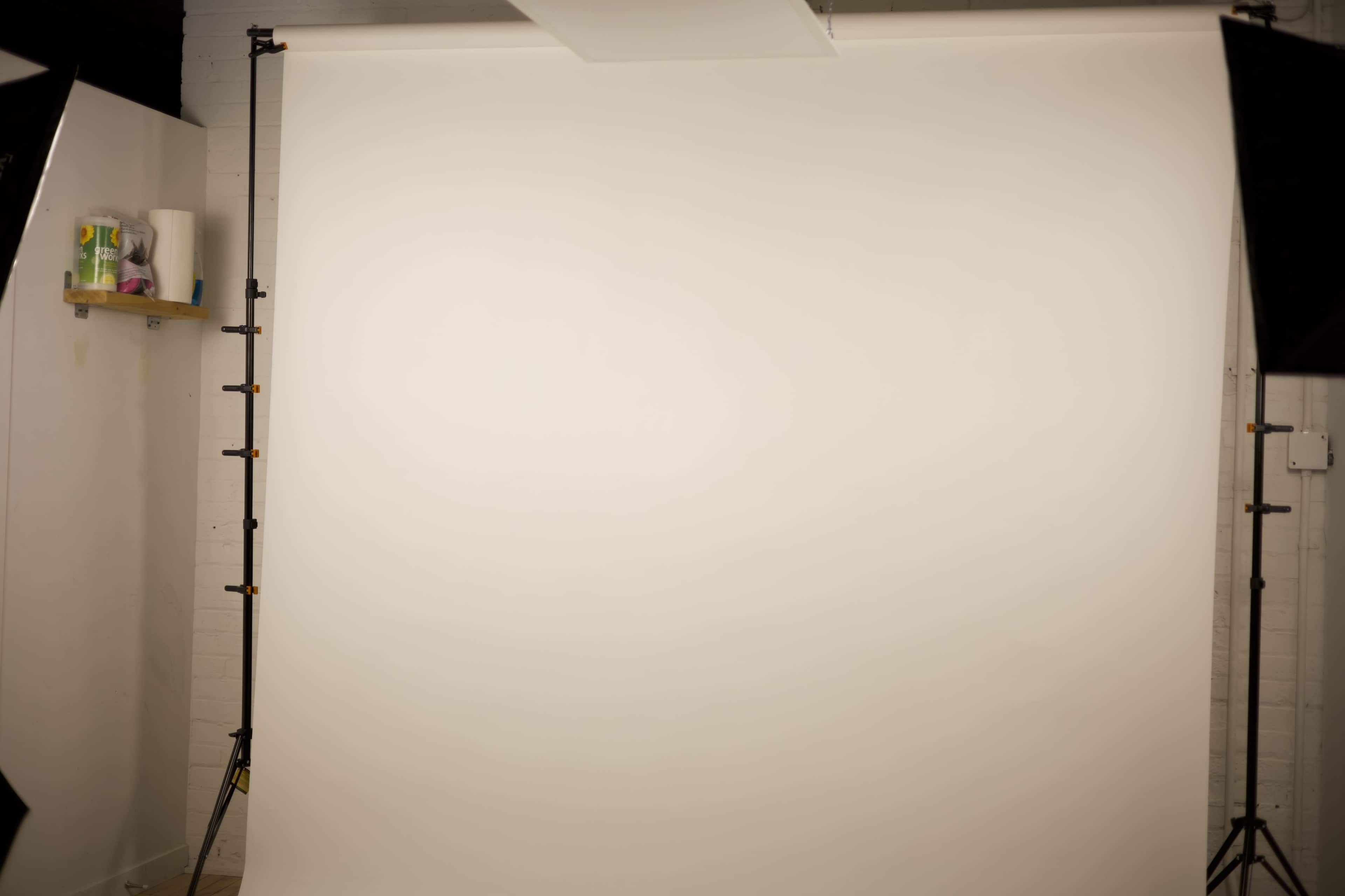 The image shows a blank, white studio backdrop with two lighting stands positioned on either side.