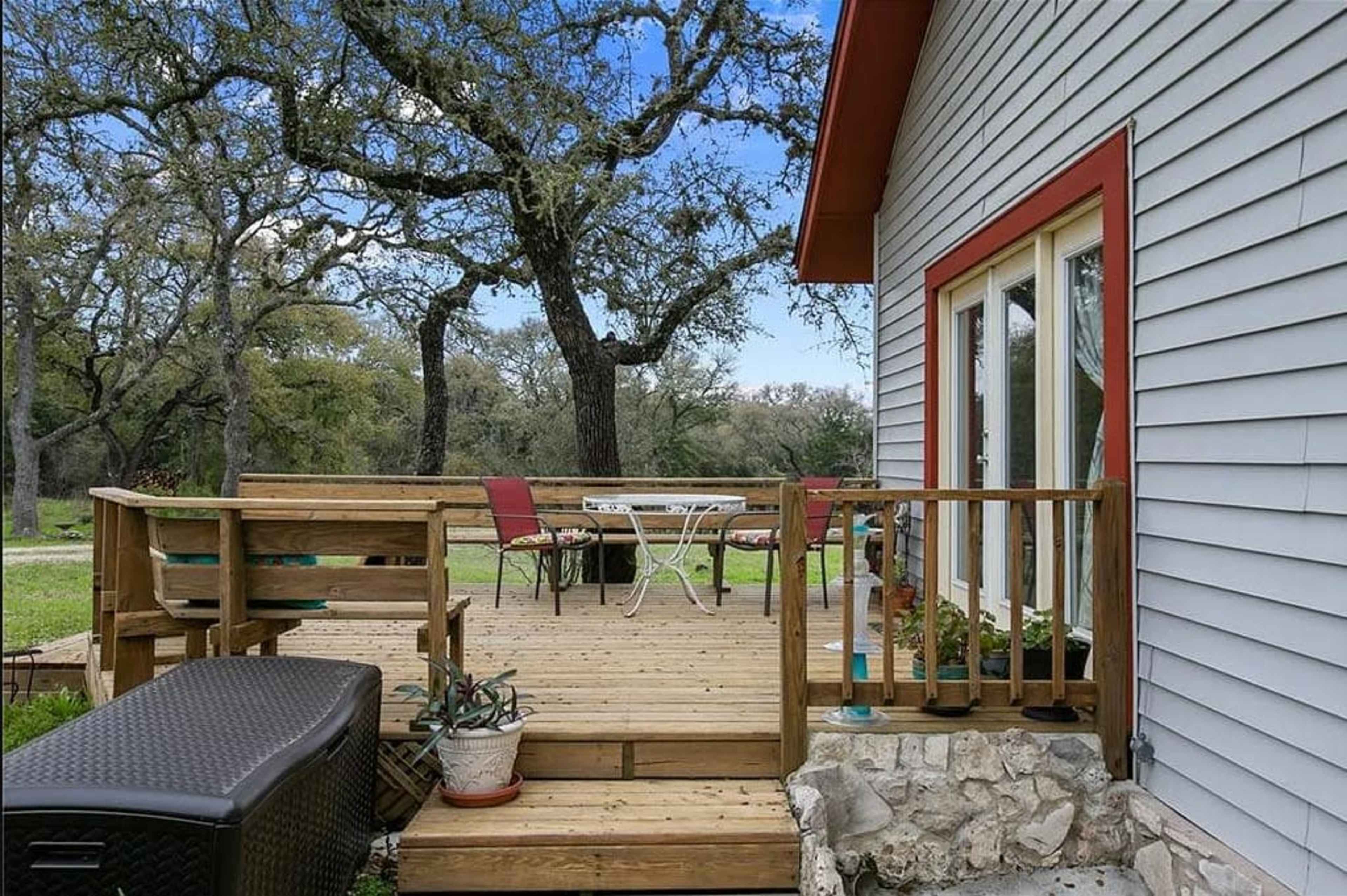 A wooden deck with outdoor furniture is attached to a house, surrounded by trees and grassy areas.