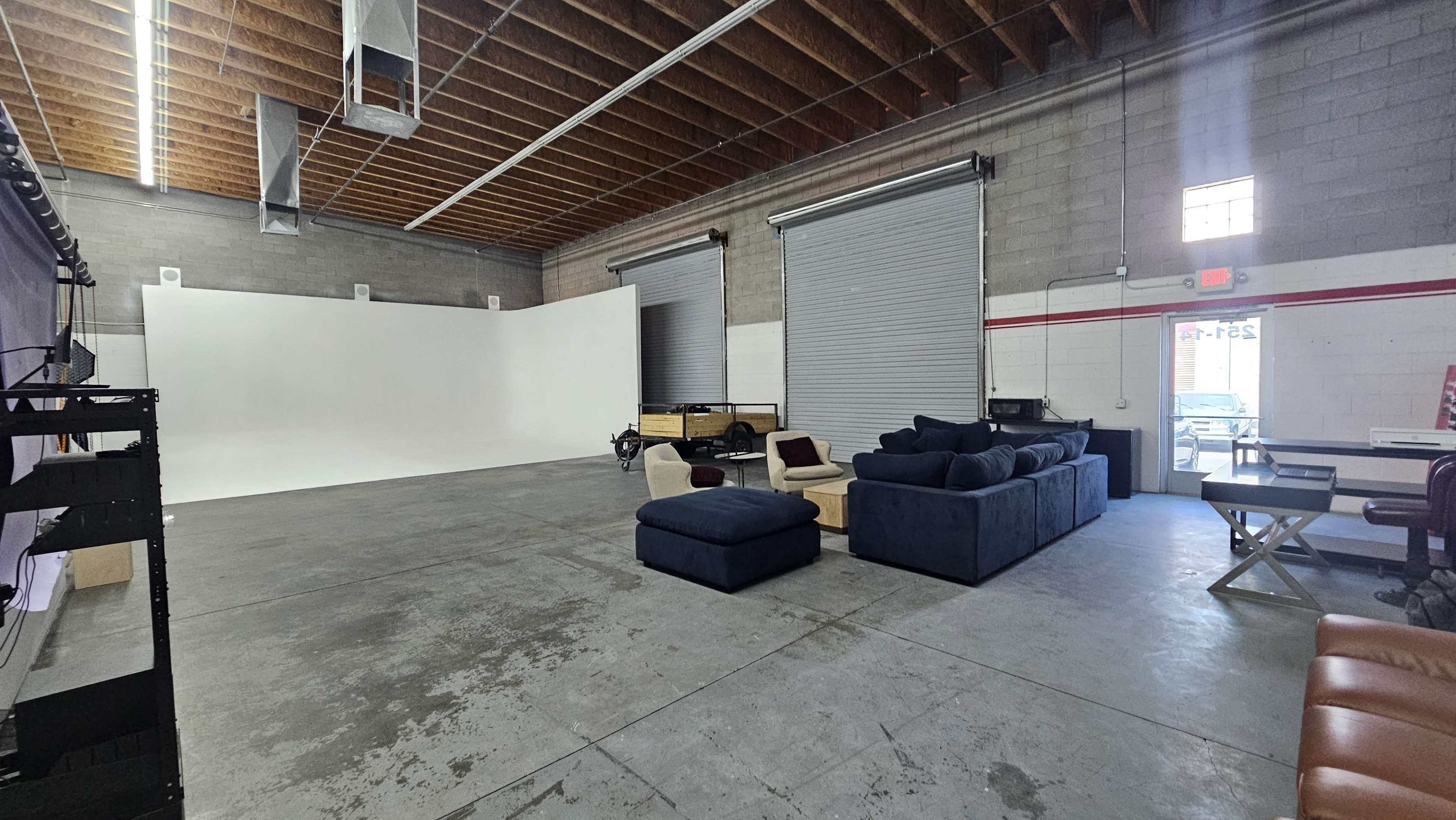 The image shows a spacious studio with concrete floors, a white backdrop on one side, and various seating options, including a large blue sofa.