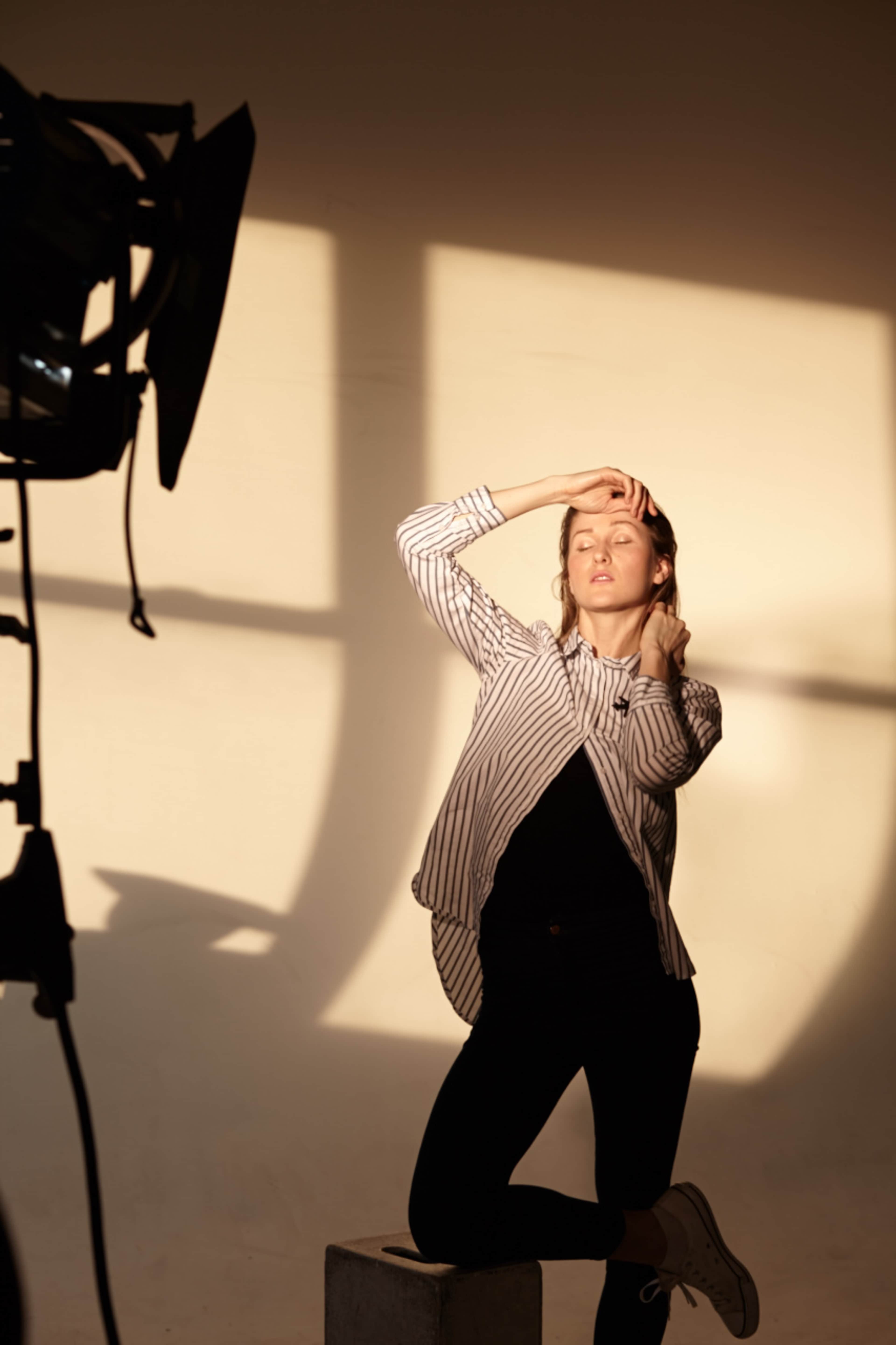 A woman poses in front of a light source, highlighting her silhouette against a plain wall.