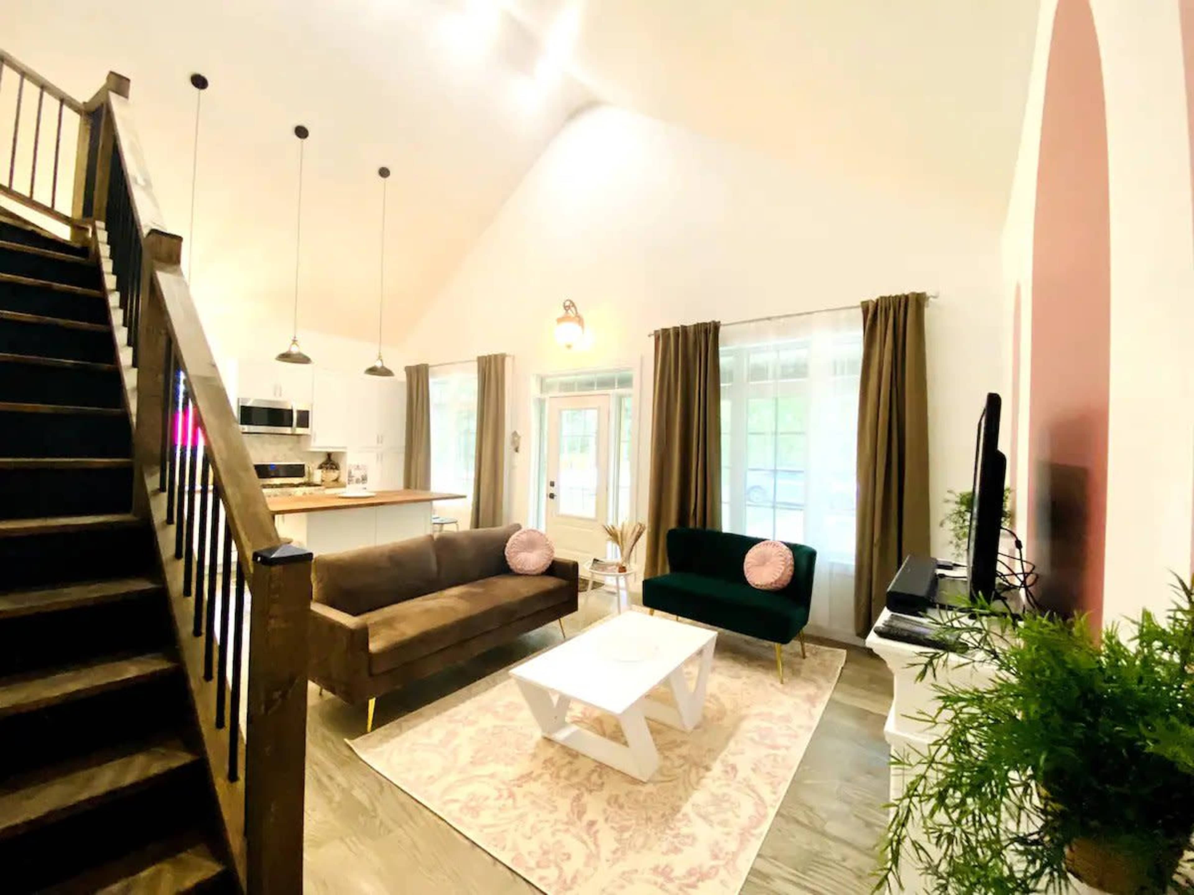 The room features a living area with a dark brown sofa, a green armchair, a white coffee table, and large windows providing natural light.