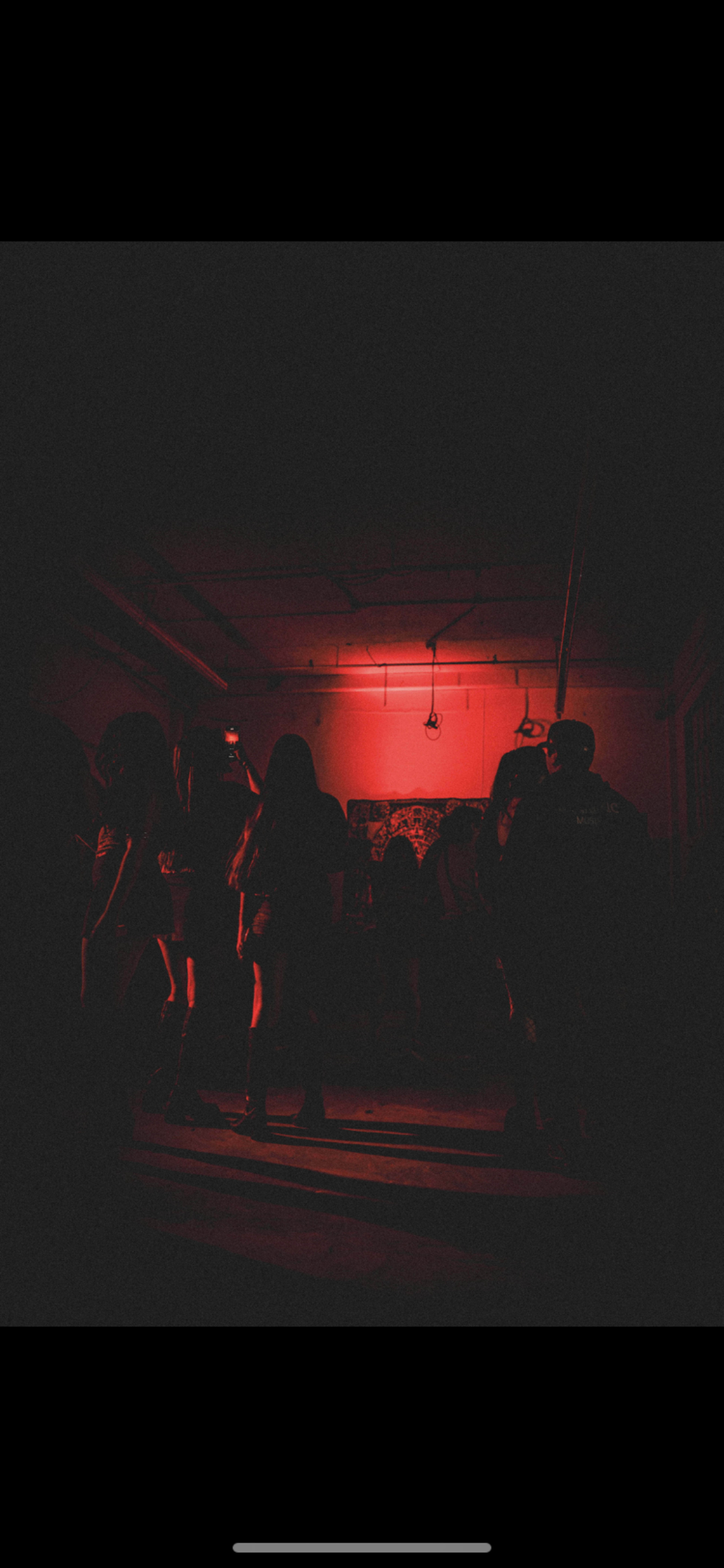 A group of people is dancing in a dimly lit room illuminated by red lights.