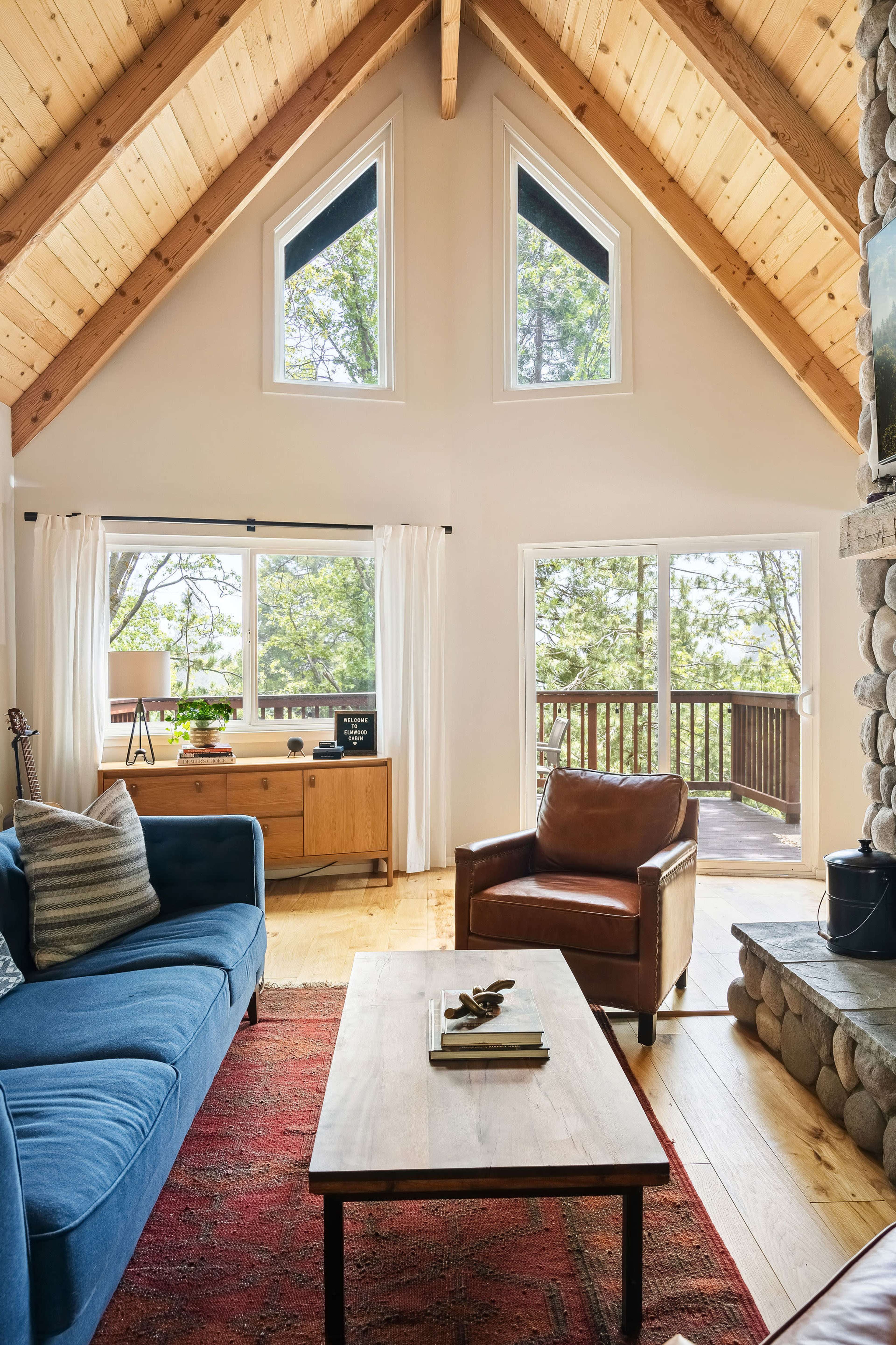 The living room features a blue sofa, a brown leather chair, a wooden coffee table, and large windows that provide a view of the outdoor area.
