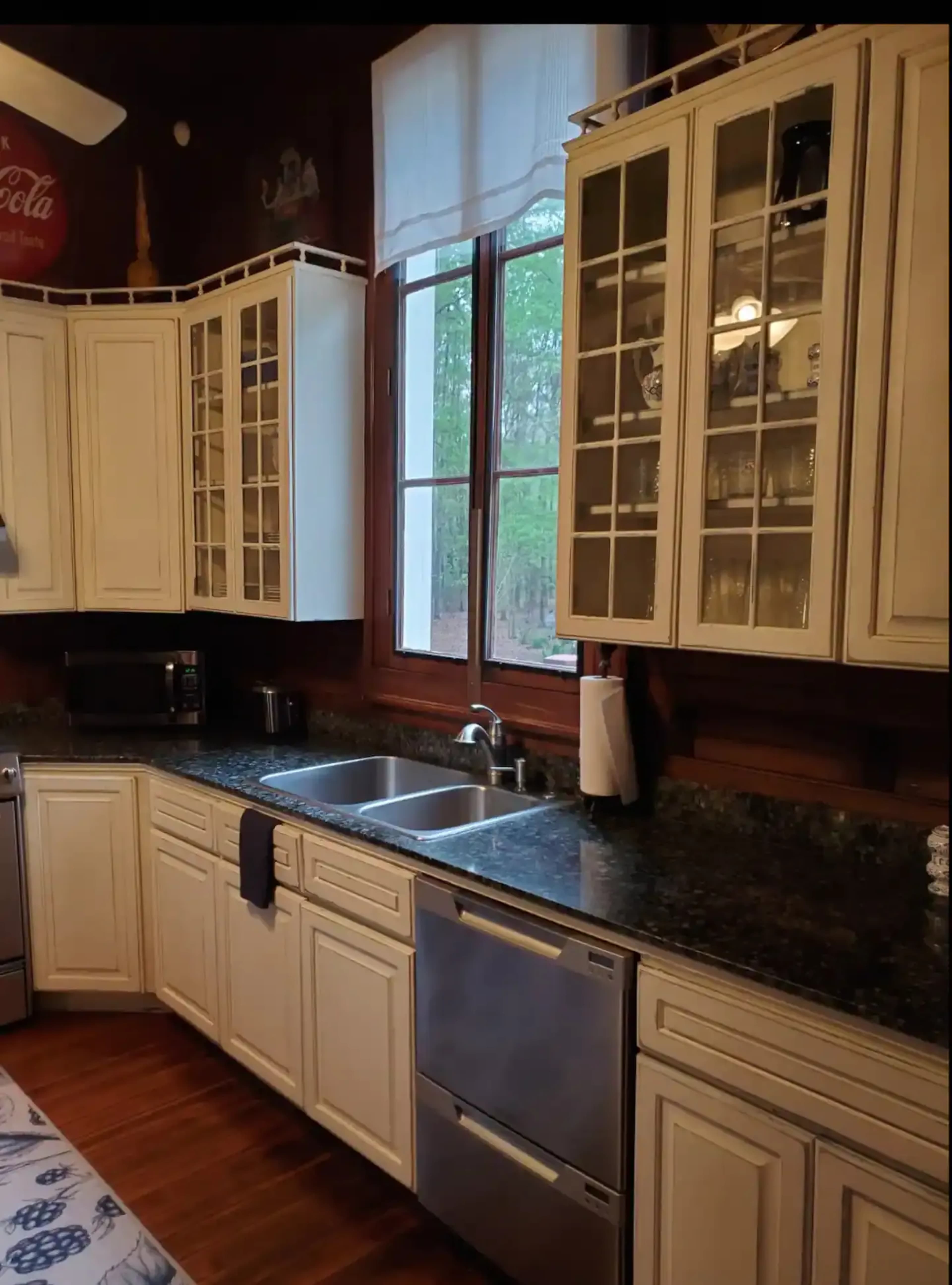 A kitchen with white cabinetry, a dark countertop, a sink below a large window, and modern appliances.