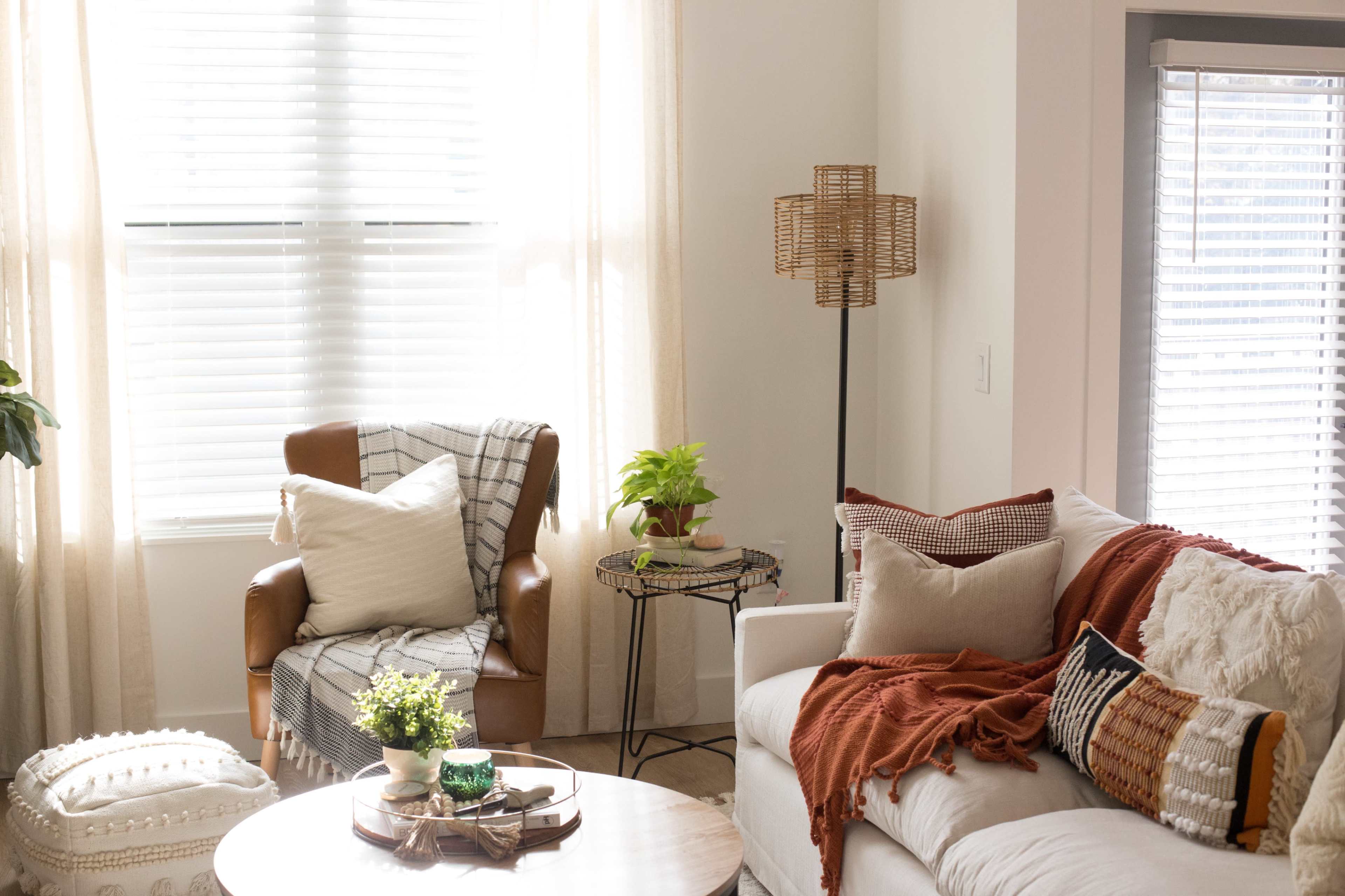 A bright living room features a comfortable chair, a side table with a plant, and a couch adorned with decorative pillows and a throw.