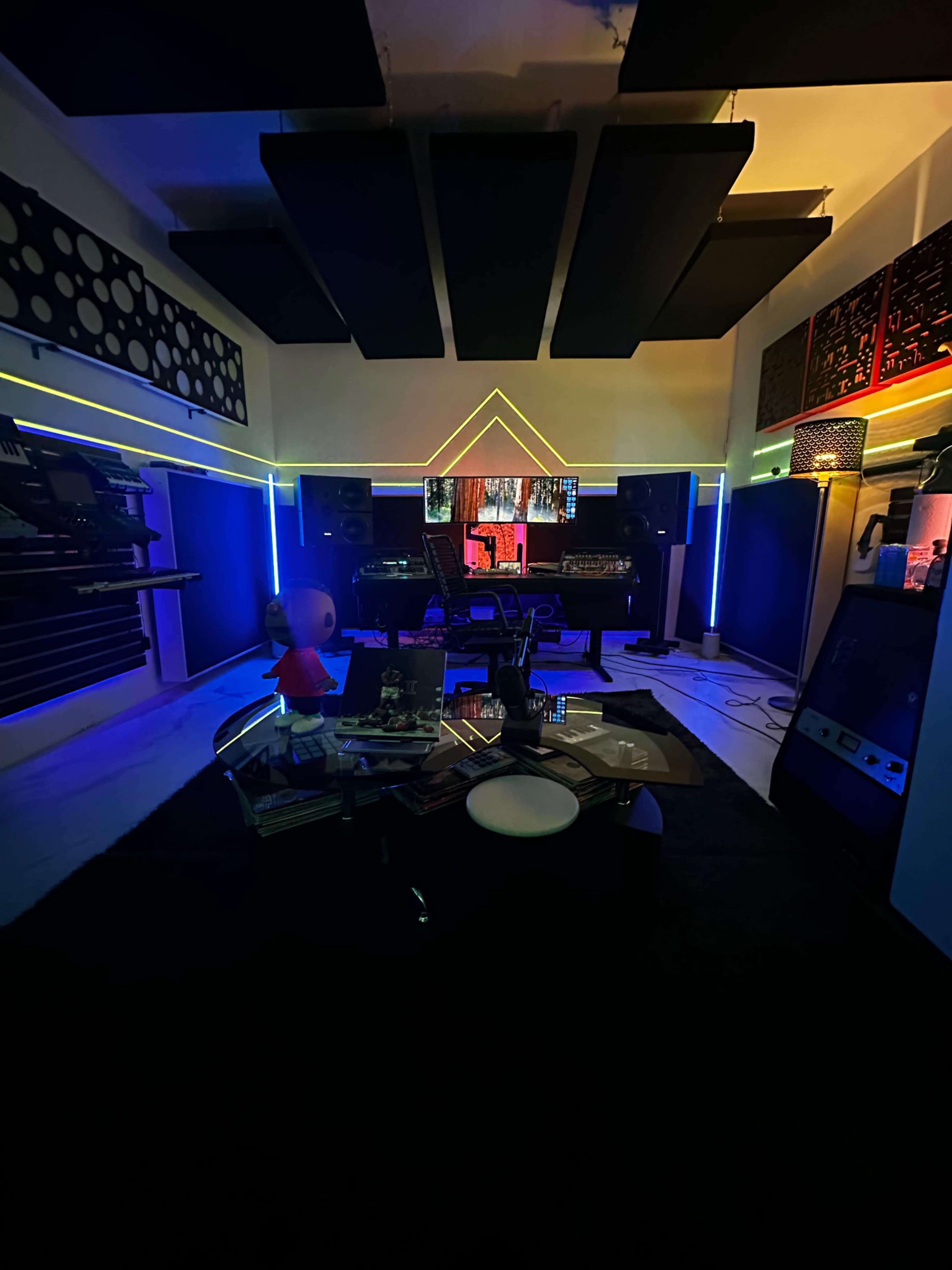 The image shows a modern music studio with colorful LED lighting, a mixing console, and various musical equipment.