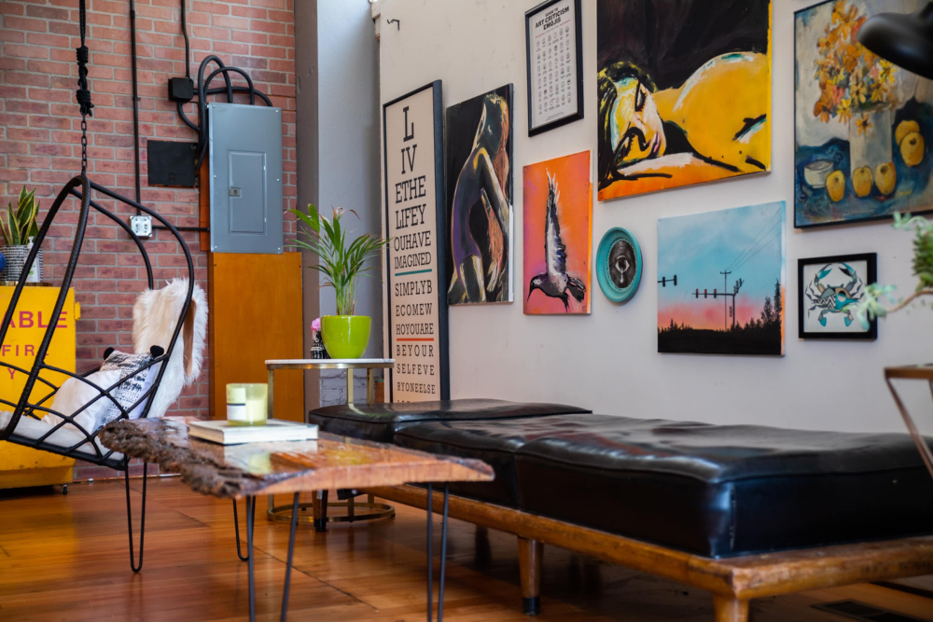 The scene features a cozy interior with a hanging swing chair, a leather sofa, and a variety of colorful artwork displayed on the walls.