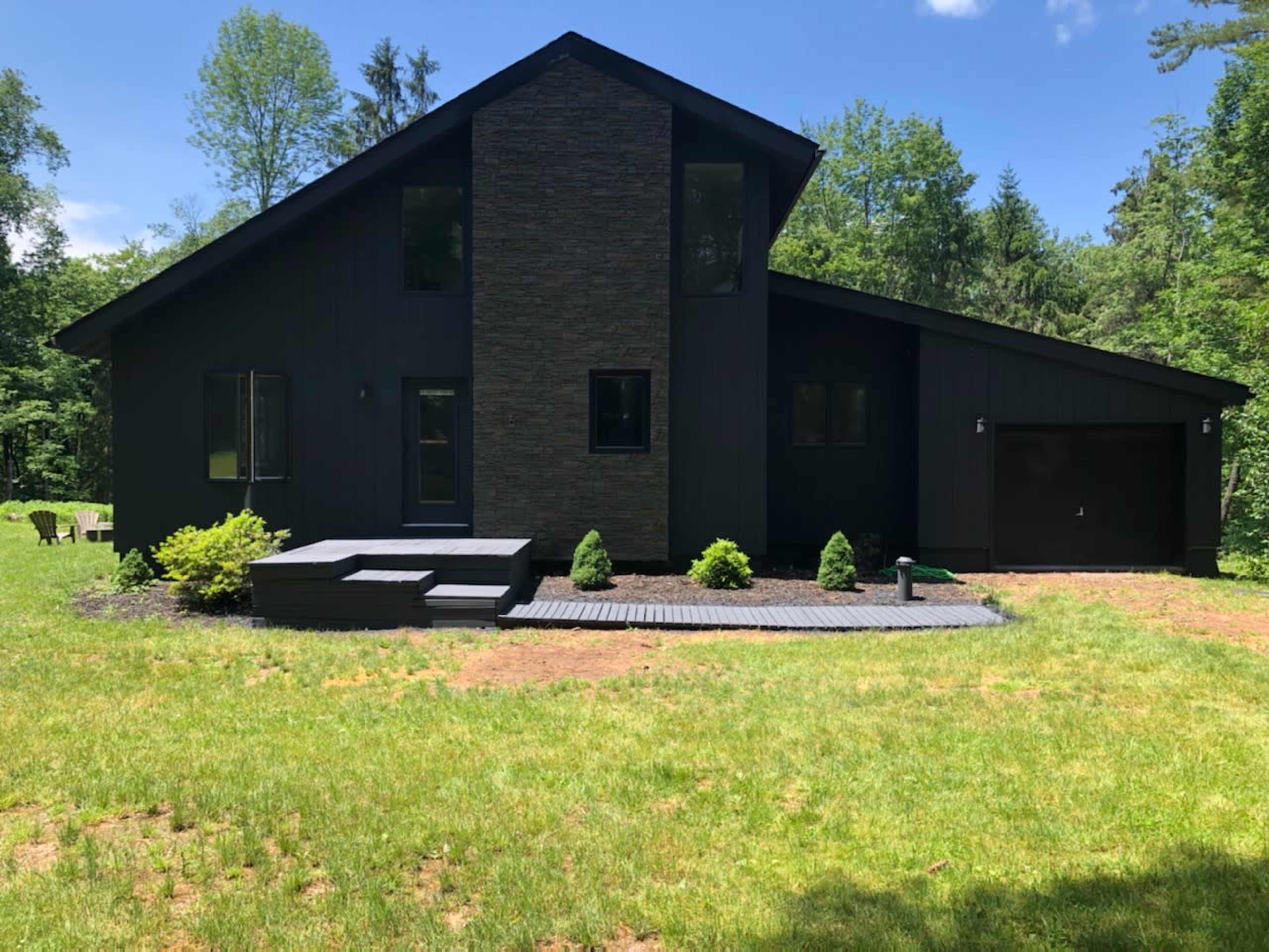A modern black house with a stone accent wall is surrounded by green grass and trees.