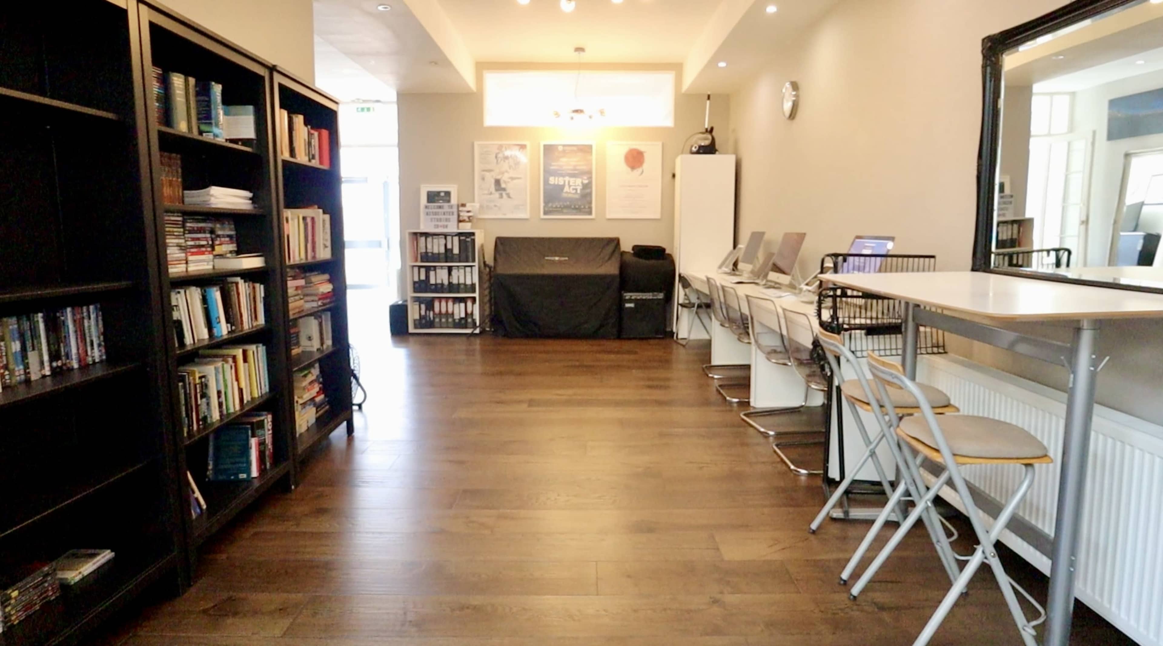 A well-lit study space features bookshelves lined with books and a row of white desks with chairs along one side.