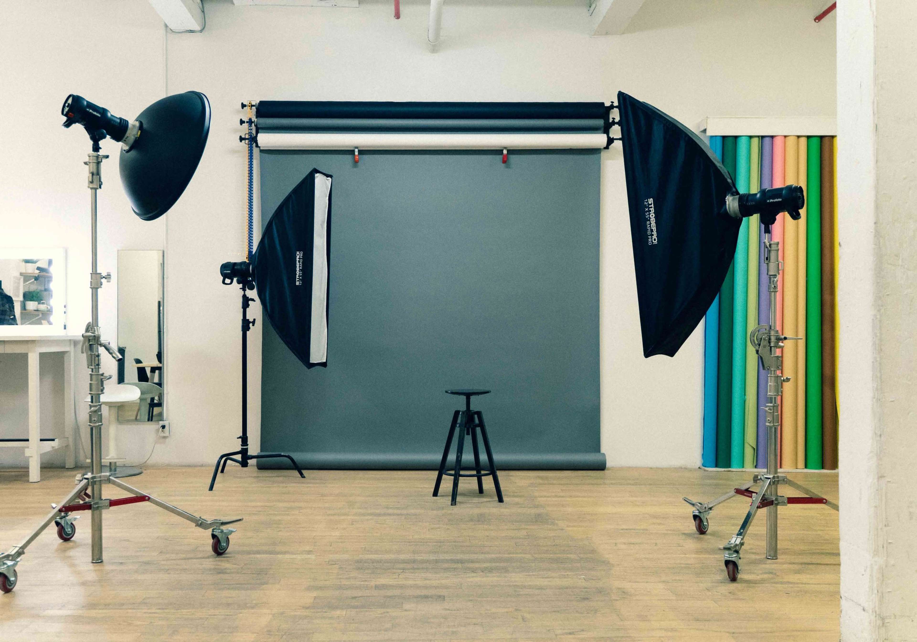 A photography studio with a gray backdrop, a stool in the center, and two softbox light setups positioned on either side.