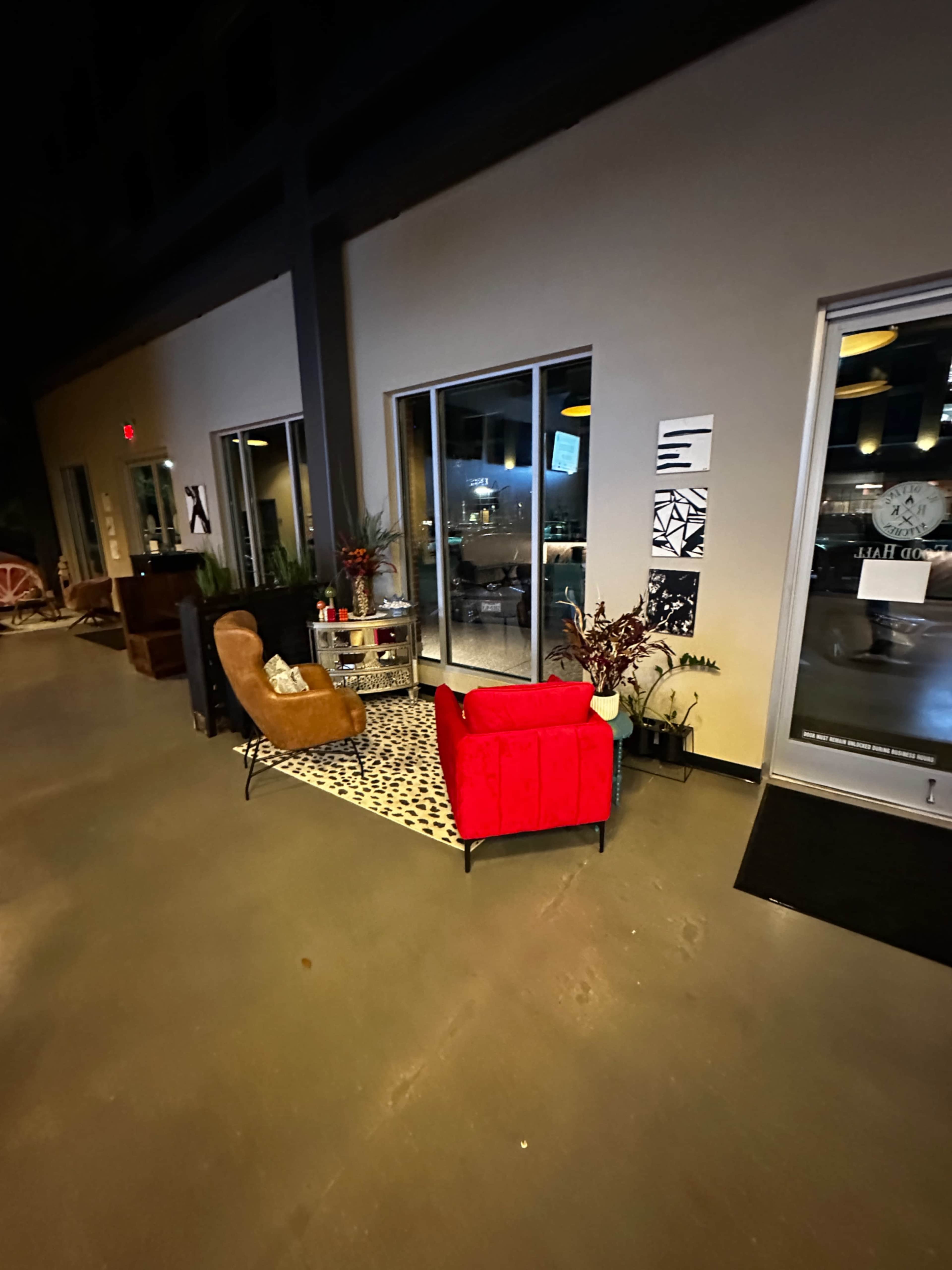 The image shows a cozy corner in a dimly lit space with a red armchair and a brown recliner, accompanied by a decorative rug and plants.