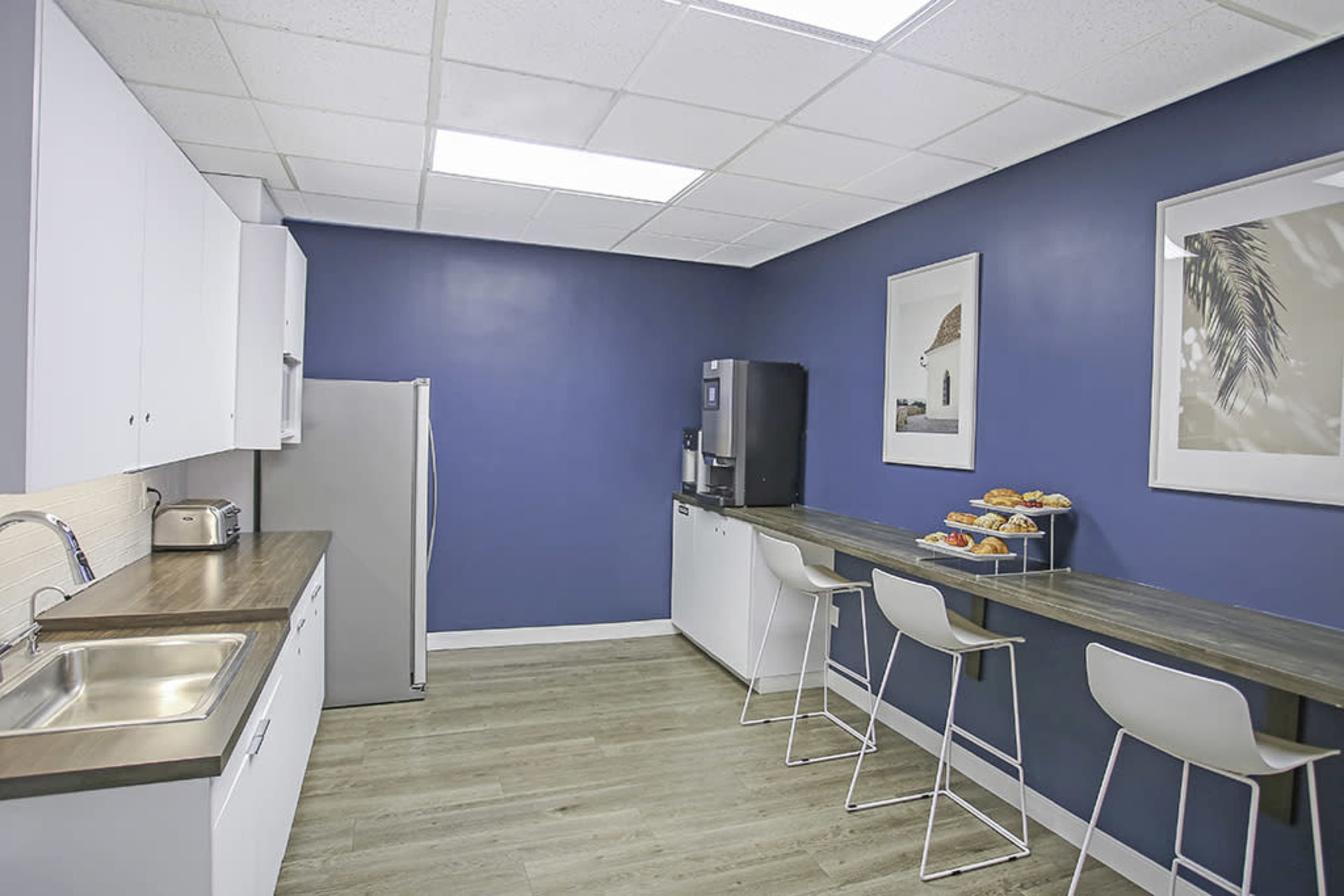The image shows a modern kitchen with white cabinetry, a stainless steel refrigerator, and a snack bar featuring a tray of pastries.