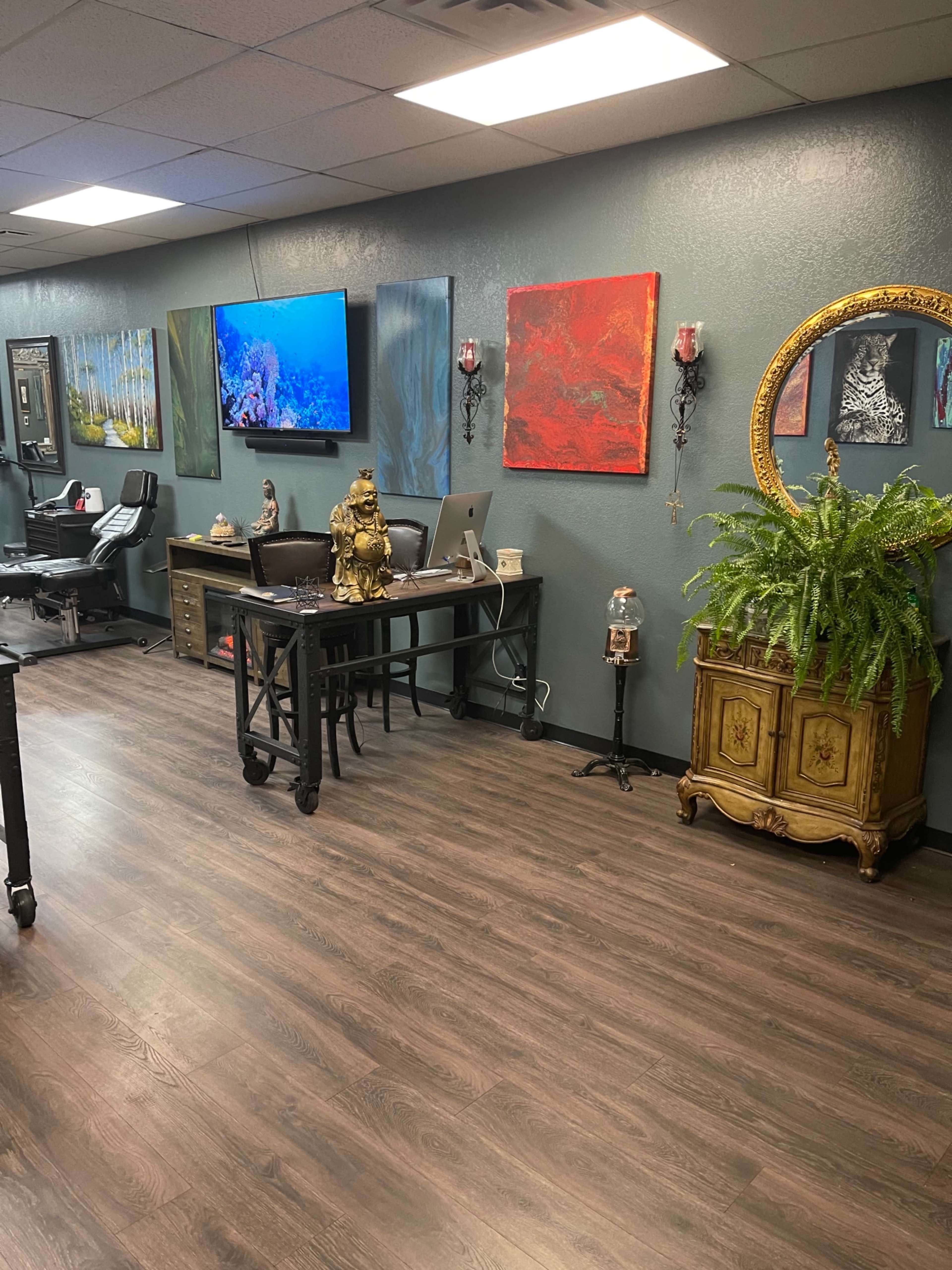 A tattoo parlor interior featuring a reception area with a desk, artwork on the walls, and a decorative plant.