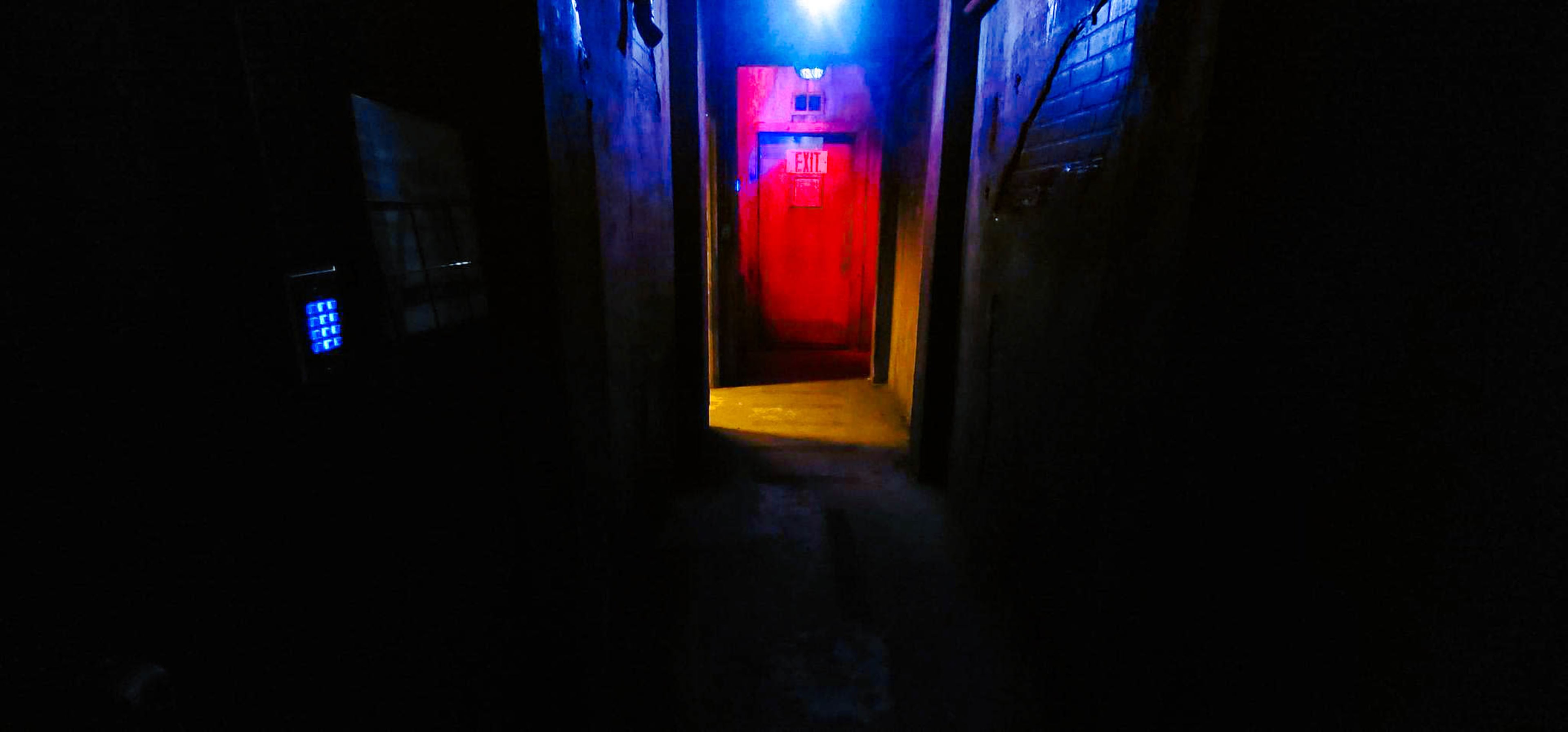 The image shows a dimly lit hallway with walls painted in dark colors, illuminated by red and blue lights at the far end.