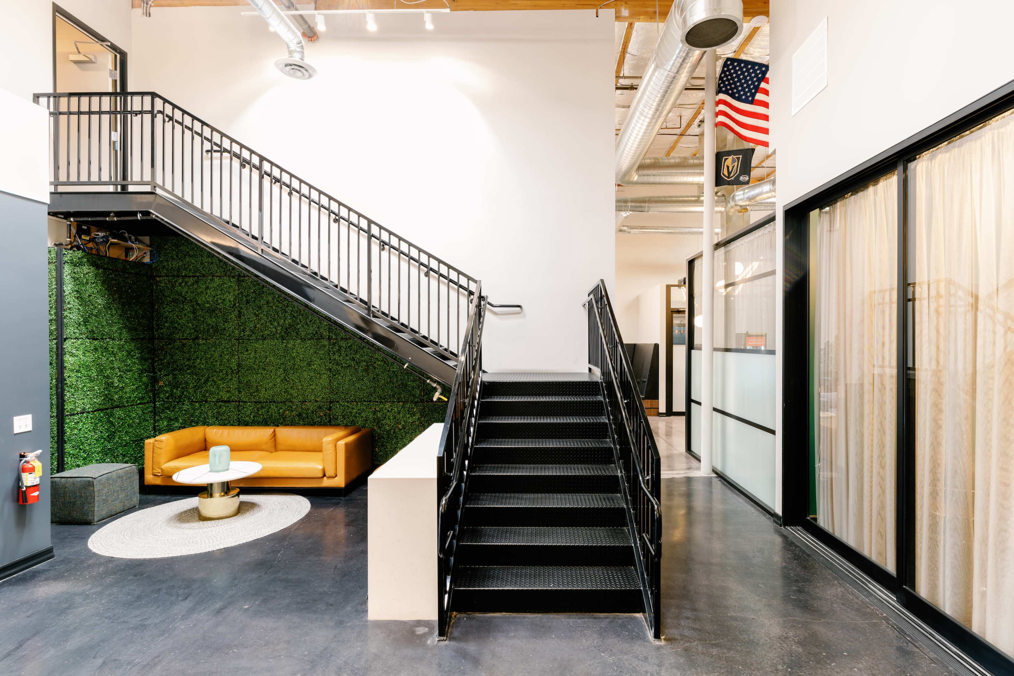 A modern interior with a staircase leading to an upper level, a green wall, and a yellow couch adjacent to a round table.
