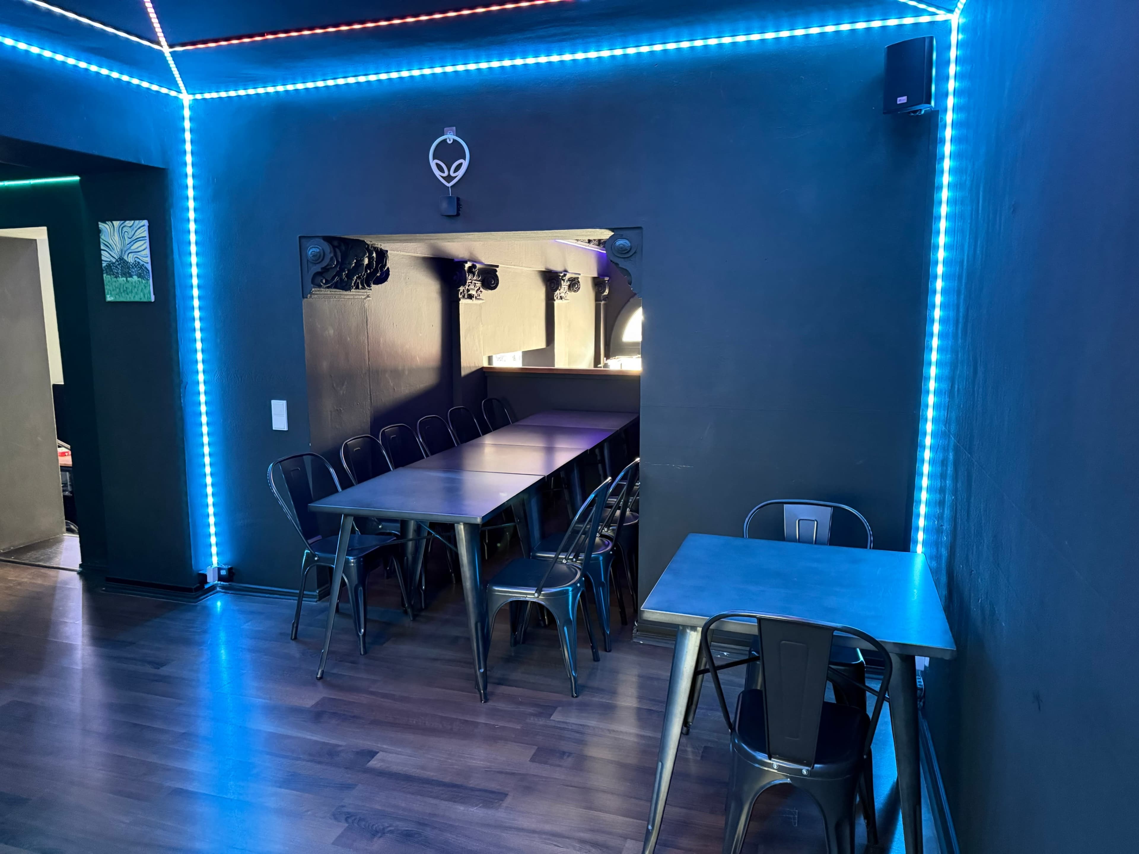The image shows a modern interior space with a long metal table surrounded by metal chairs, illuminated by neon blue lighting along the walls.