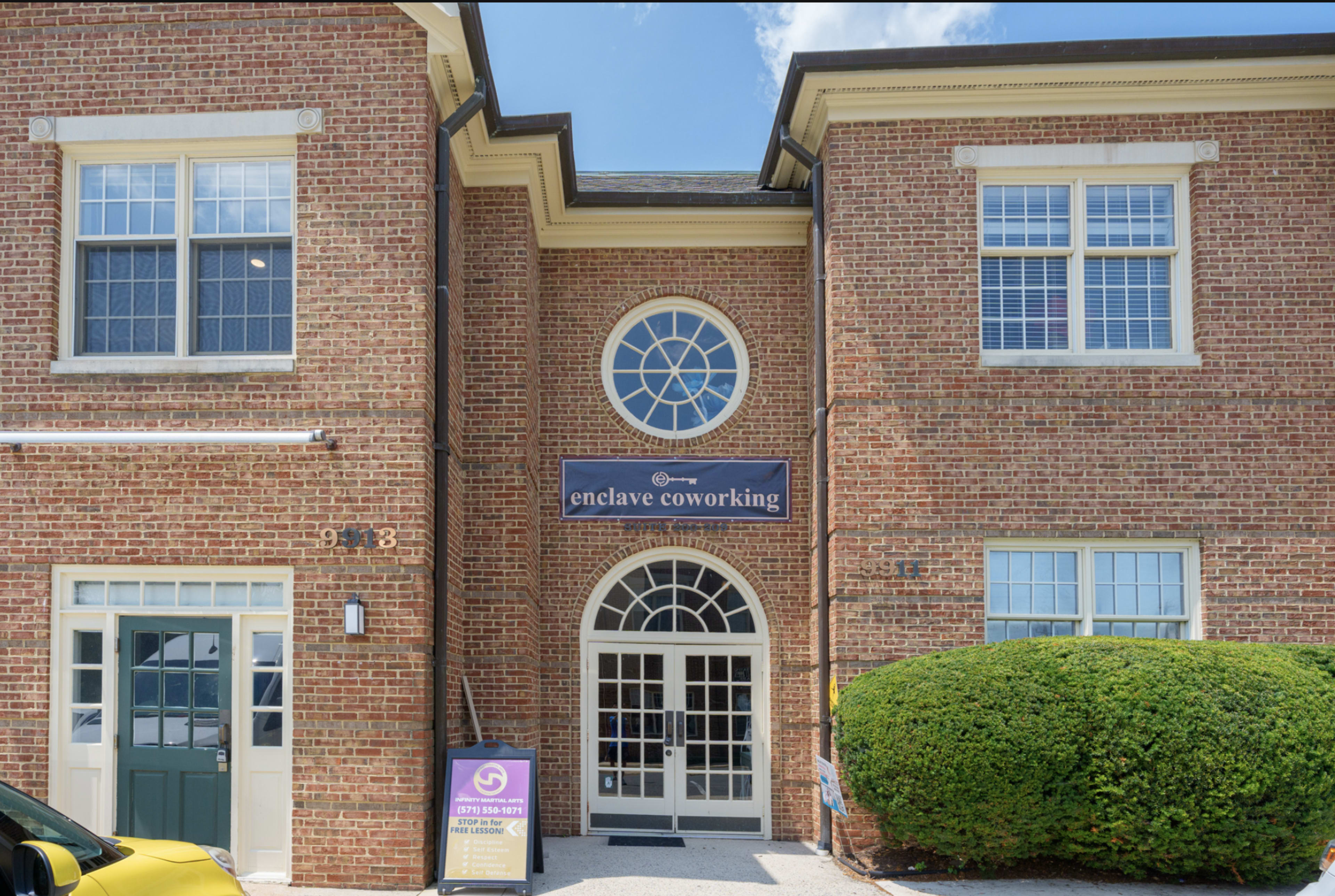The image shows a brick building with a sign reading "enclave coworking" above the entrance, which features a large circular window.