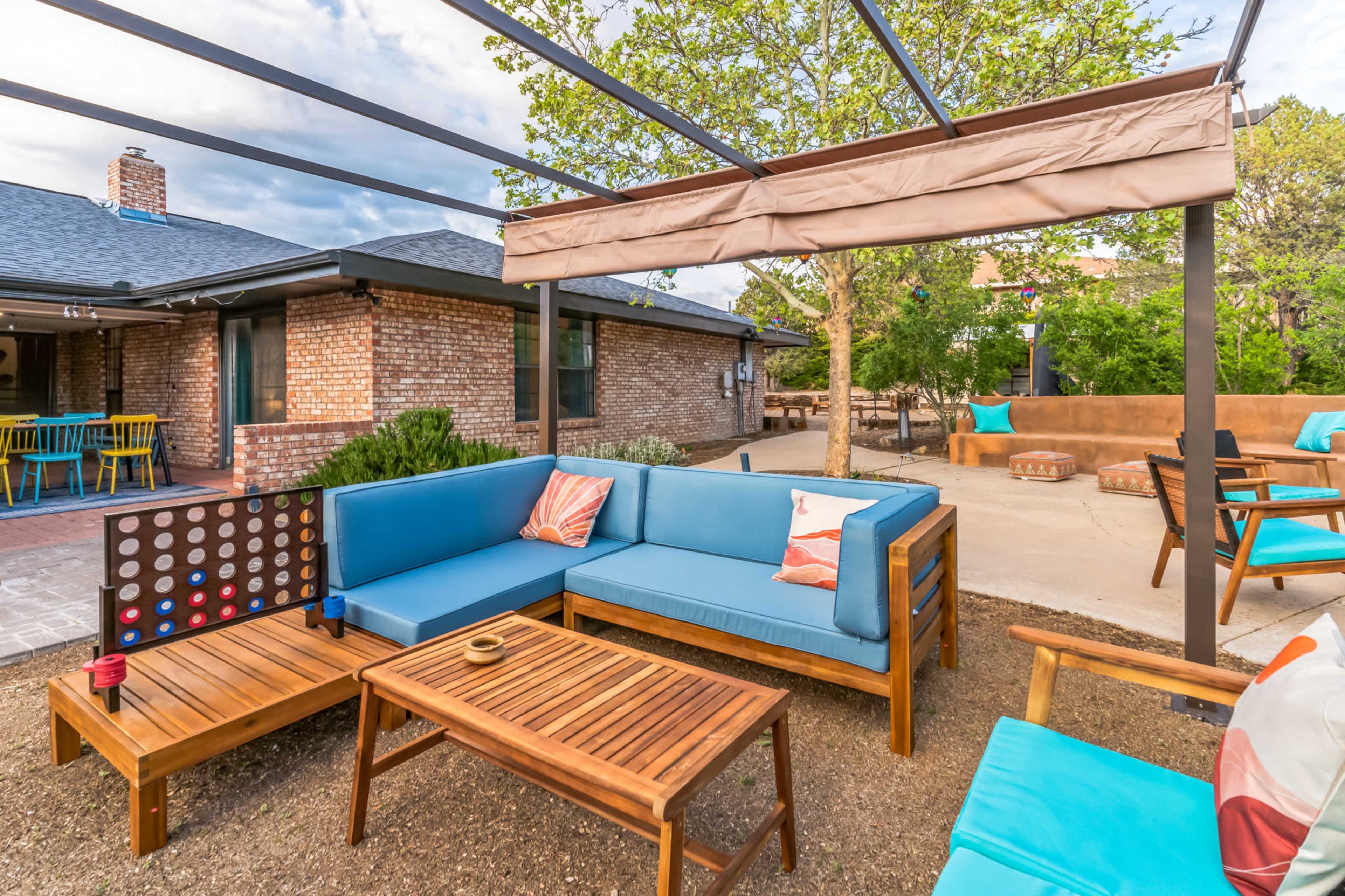 A modern outdoor seating area with a blue sectional sofa, wooden coffee table, and shaded pergola in a landscaped backyard.