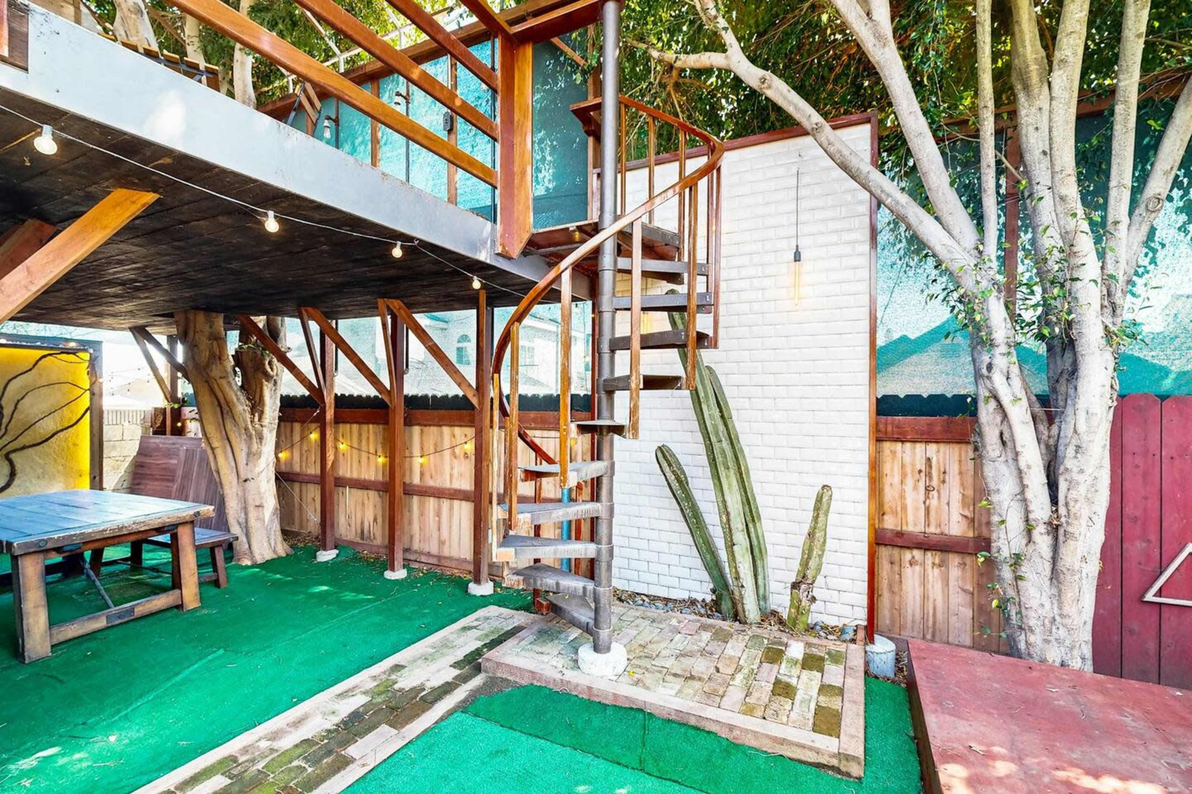A spiral staircase leading to an elevated platform in an outdoor space with wooden structures, green turf, and wall murals.