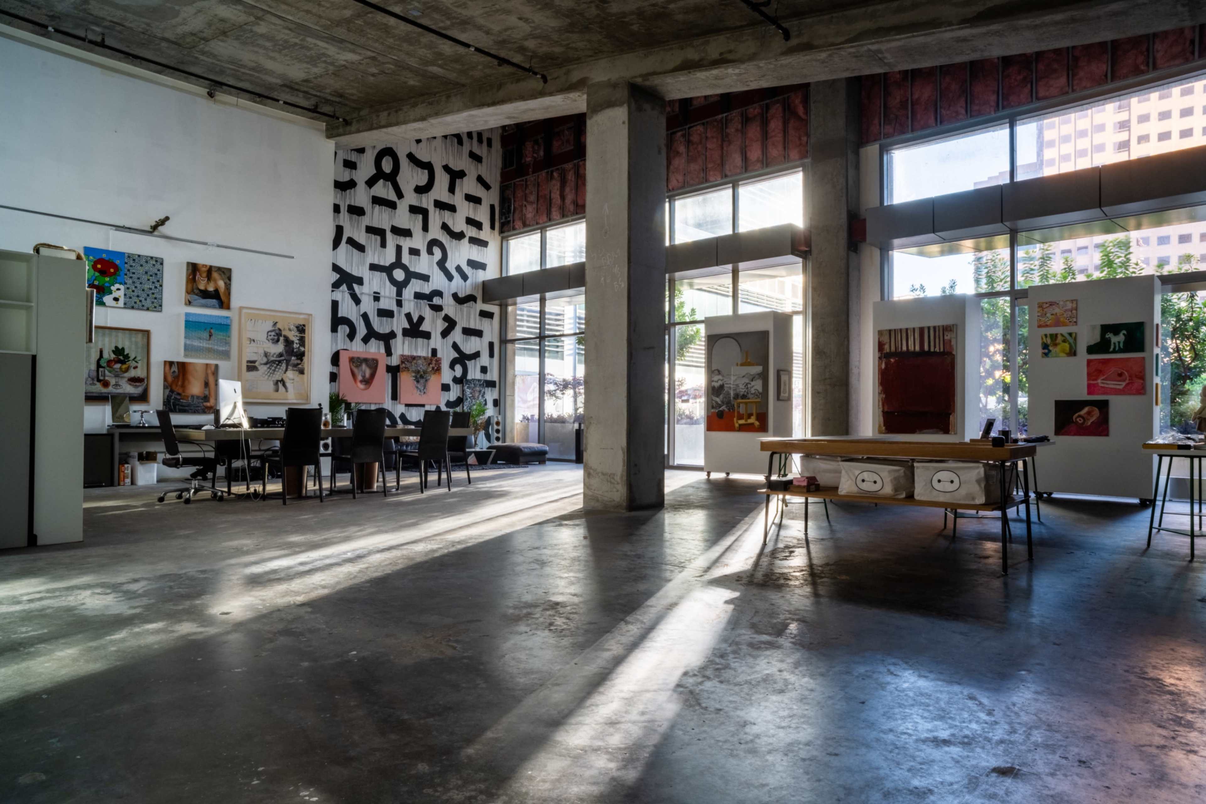 The spacious interior features an art studio with various artworks displayed alongside a meeting area equipped with black chairs and a large table.