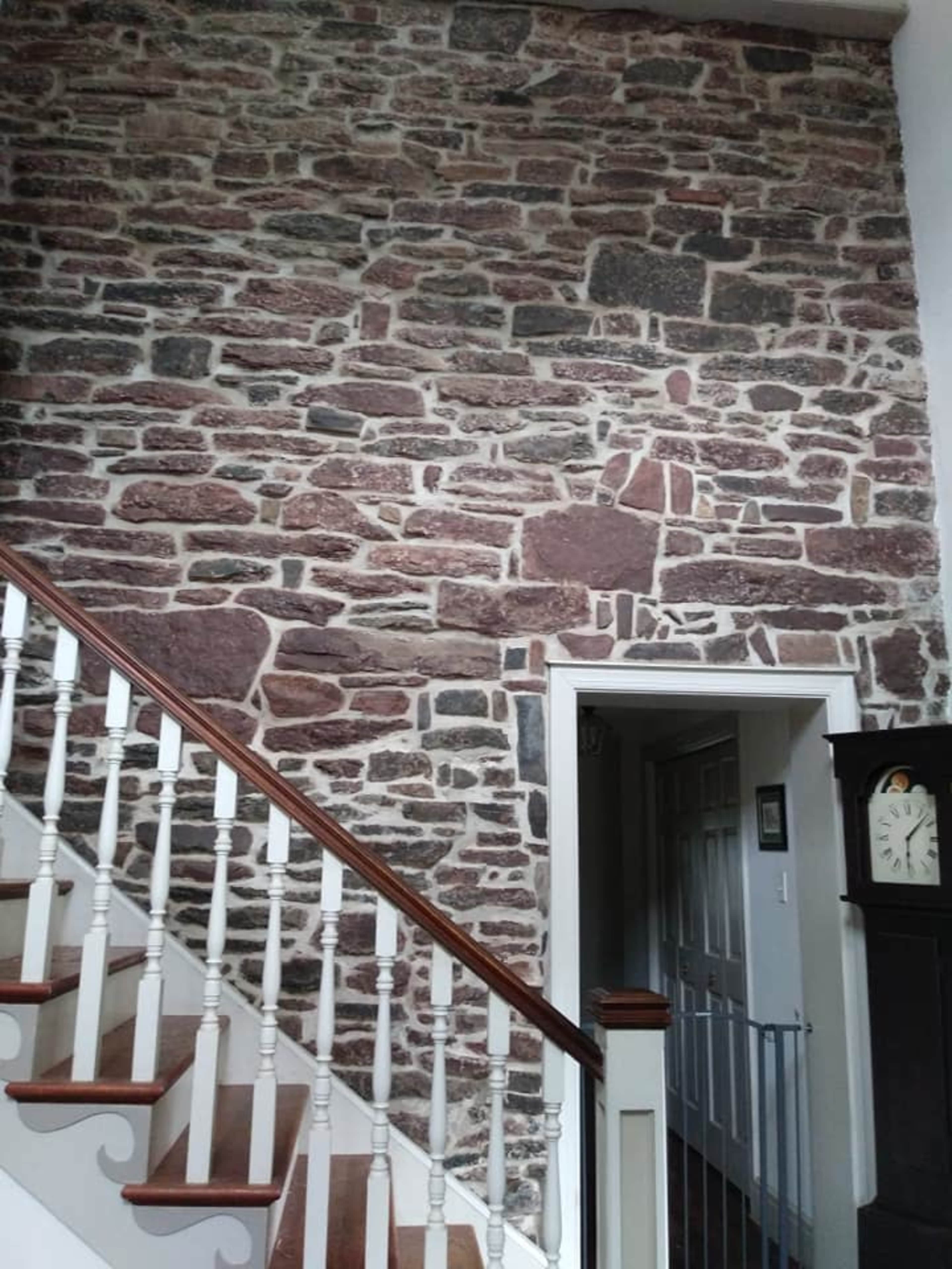 A stone wall with a staircase railing beside it, leading to a doorway.