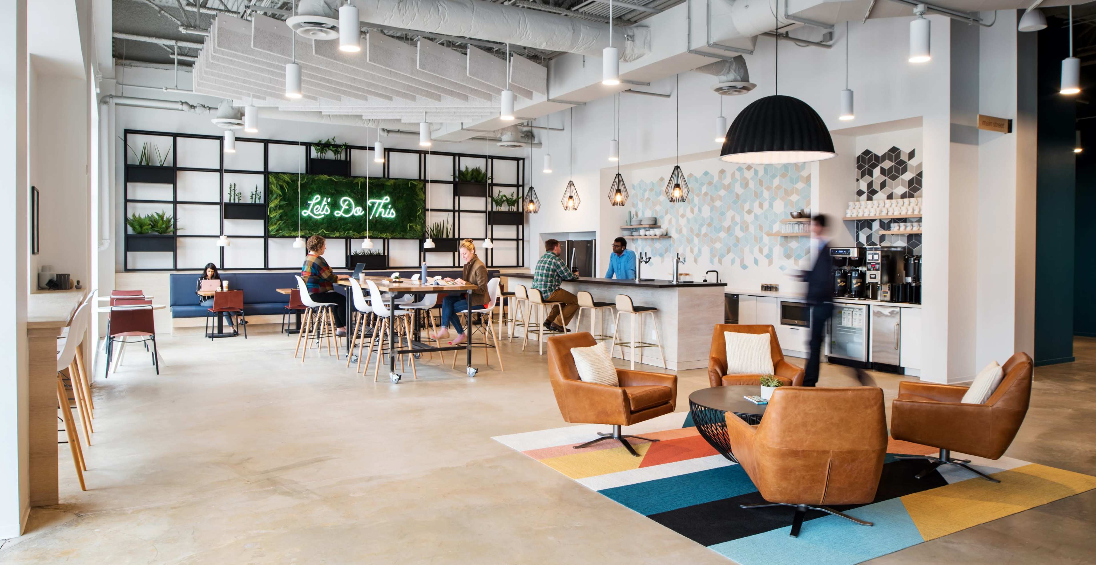 A modern office space with a seating area, a café-style bar, and decorative plants on shelves.